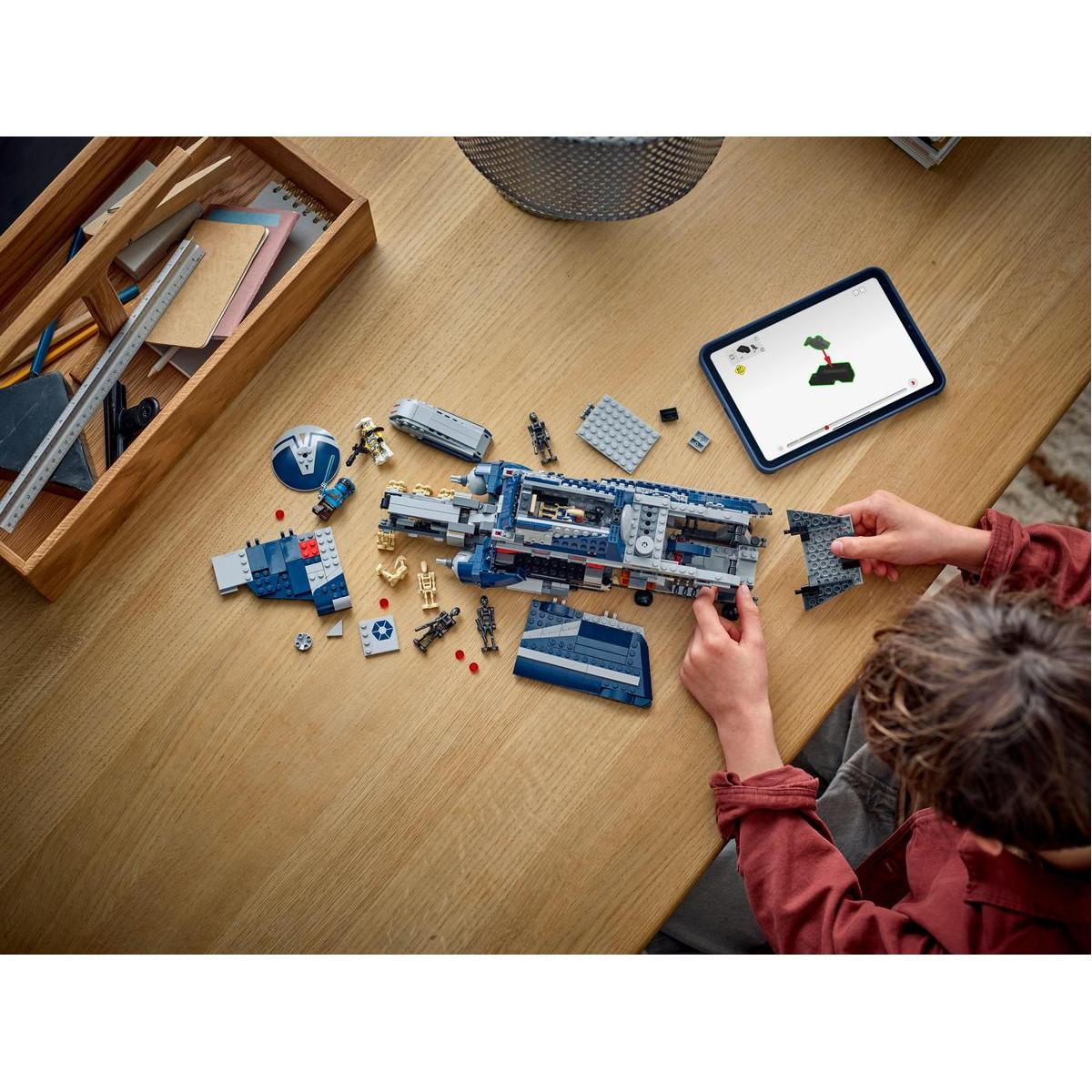 Dziecko składa statek Lego Star Wars na drewnianym stole, z akcesoriami i instrukcjami.