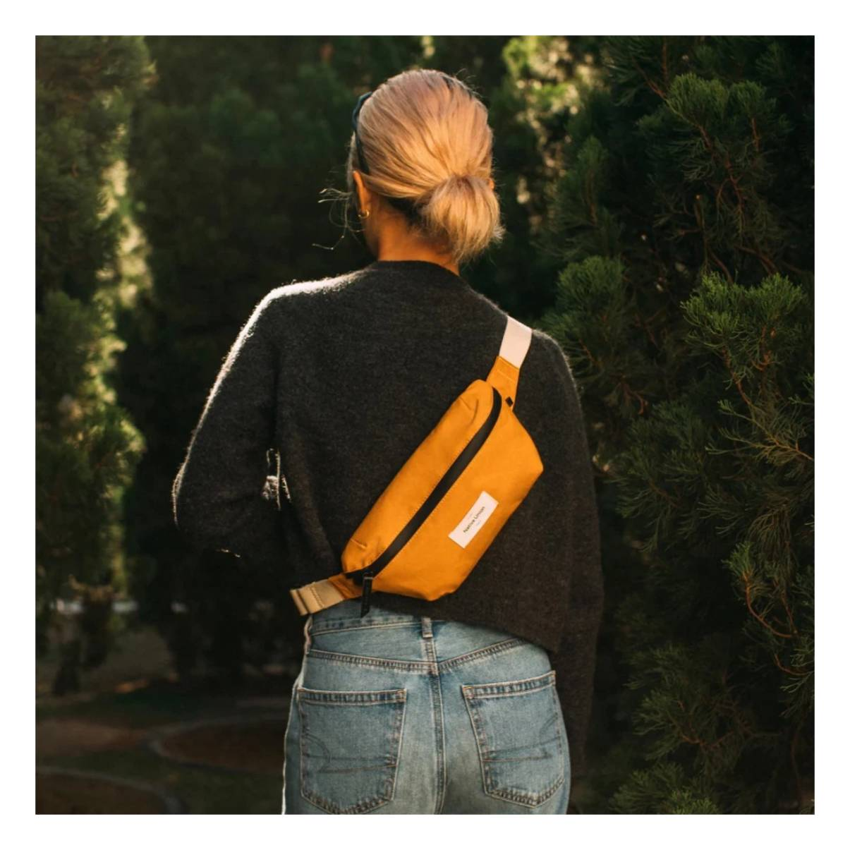 Una donna indossa un maglione grigio e jeans, con un marsupio giallo senape sulla schiena.