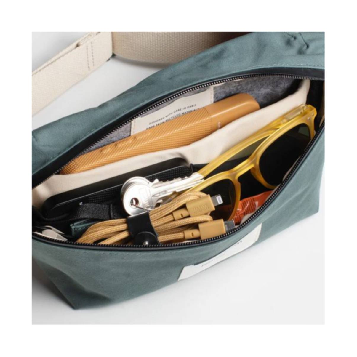 Borsa teal aperta con contenuto: occhiali da sole, chiavi, cavi e una penna.