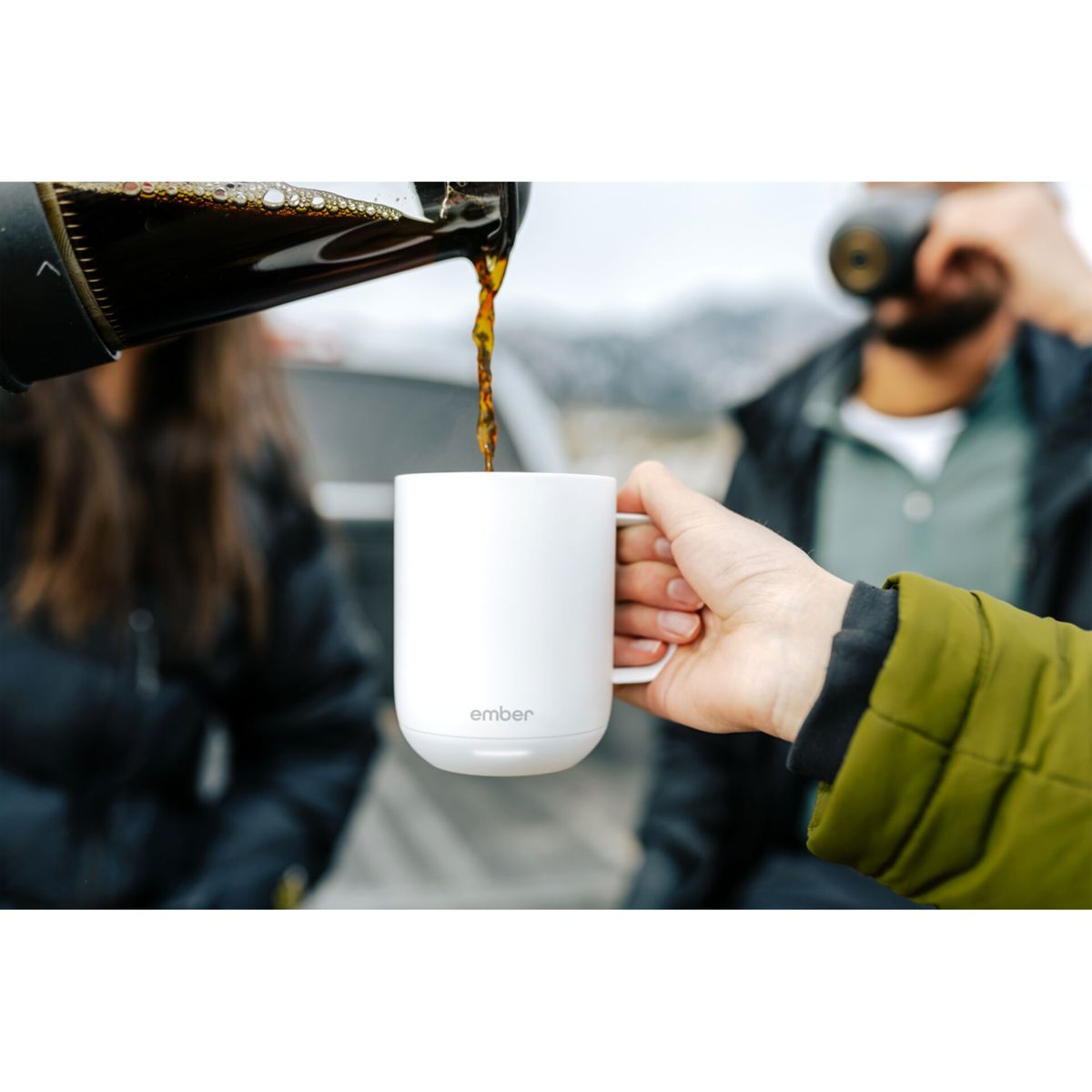 Caffè versato in una tazza bianca. Mano di un uomo che tiene la tazza, altra persona sullo sfondo.