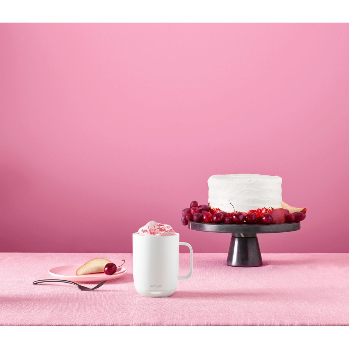 Una tazza bianca con panna montata e una torta con uva su sfondo rosa.