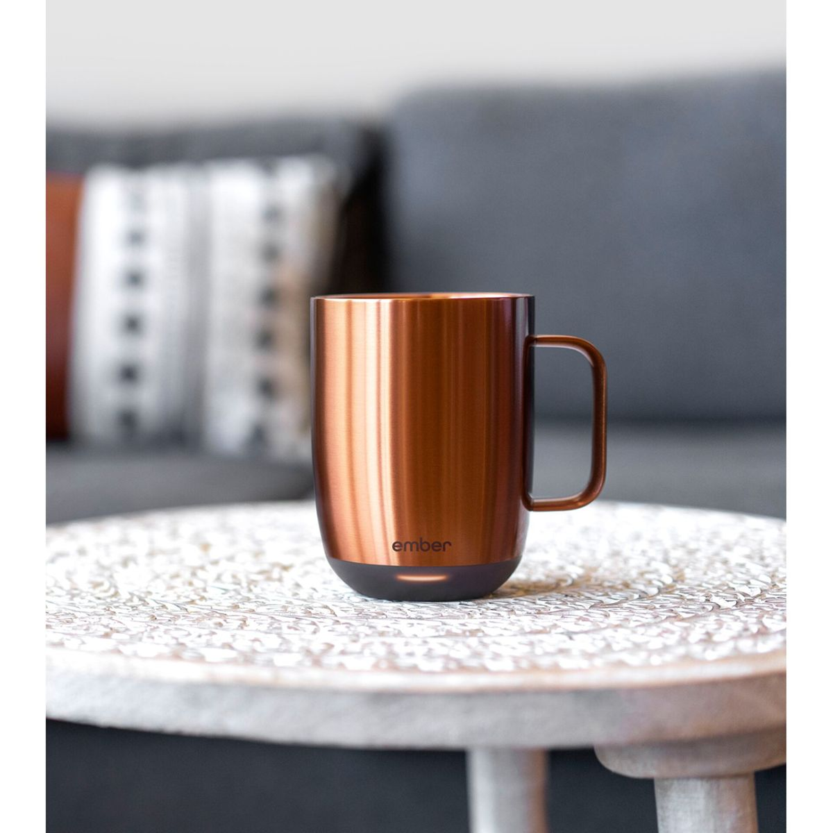 Tazza color rame su un tavolo bianco. Lo sfondo è una messa a fuoco morbida di uno spazio interno.