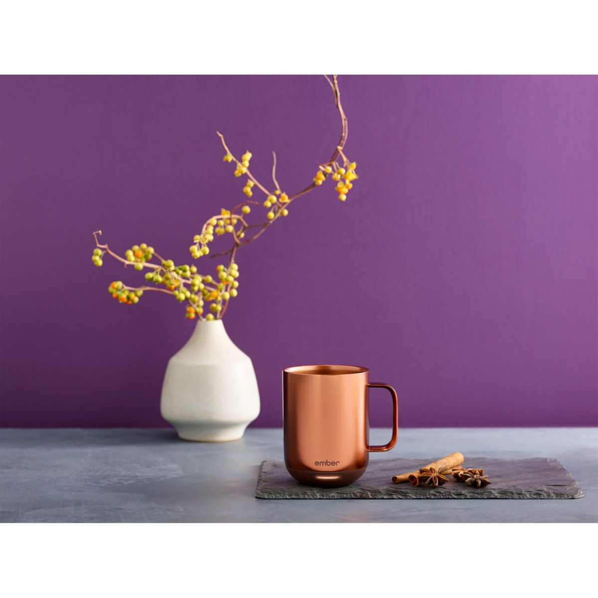Tazza di rame con spezie su un'ardesia. Vaso con fiori gialli sullo sfondo. Parete viola.