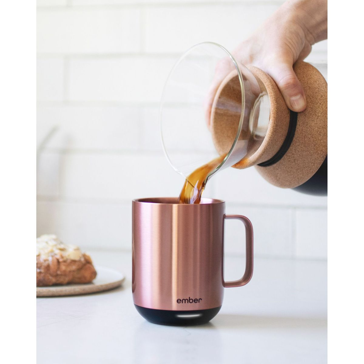 Caffè versato in una tazza color oro rosa da una caraffa di vetro. Sfondo bianco.