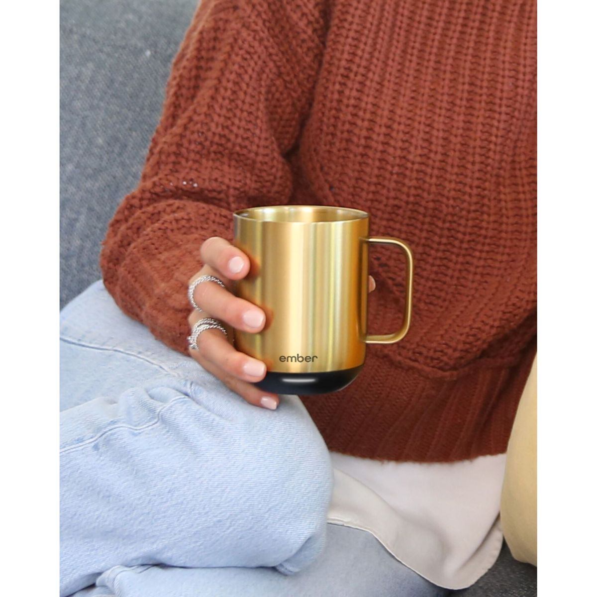 Person sitzt und hält eine goldene Tasse mit dem Wort 'ember' darauf.