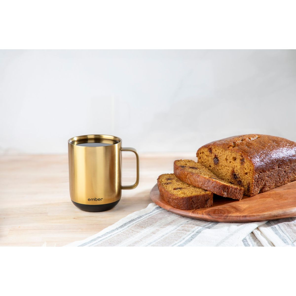 Goldener Becher neben einem geschnittenen Brotlaib auf einem Holzbrett. Das Brot hat Rosinen und eine Kruste.