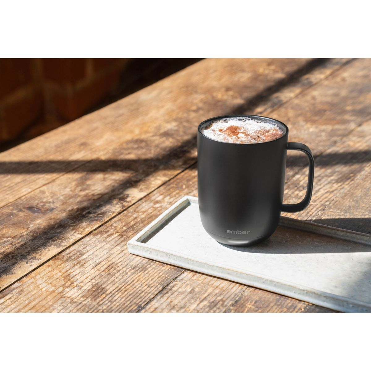 Tazza nera con schiuma su un tavolo di legno. Un vassoio rettangolare è sotto la tazza. Lo sfondo è sfocato.