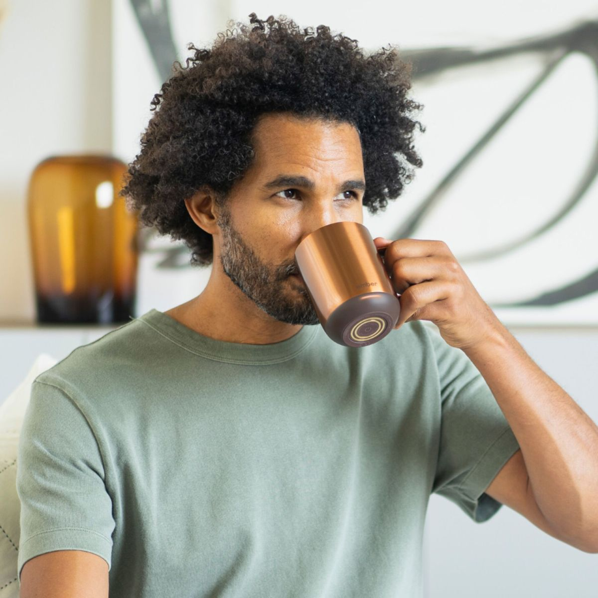 Un uomo beve da una tazza di rame. Un dipinto e un vaso sullo sfondo.