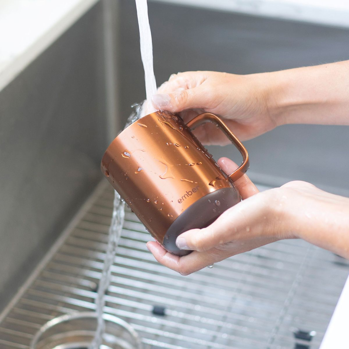 Mani che lavano una tazza di rame sotto l'acqua corrente in un lavandino d'acciaio. La tazza è bagnata e lucida.