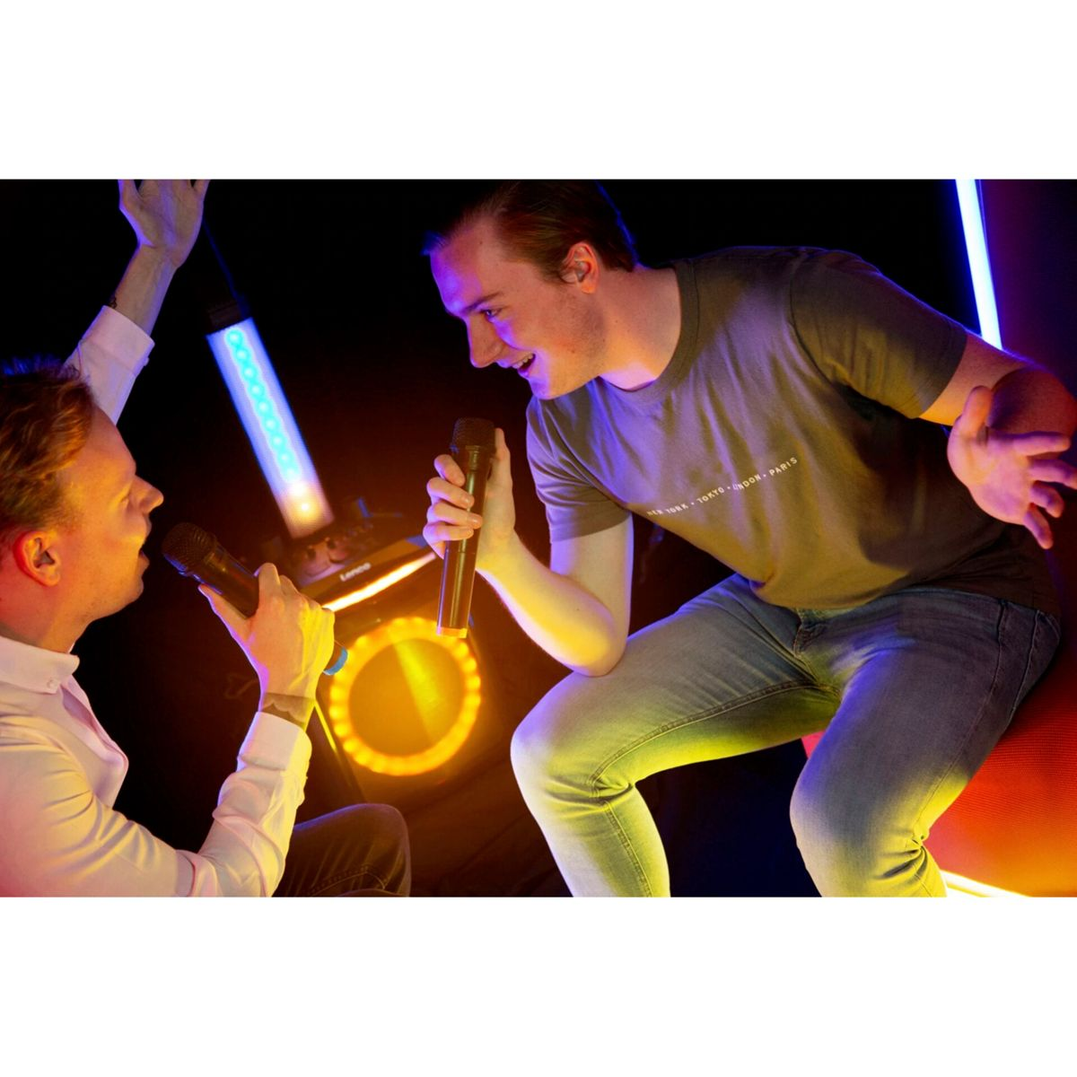 Dwóch mężczyzn śpiewa do mikrofonów, oświetlonych światłami scenicznymi. Jeden gestykuluje.