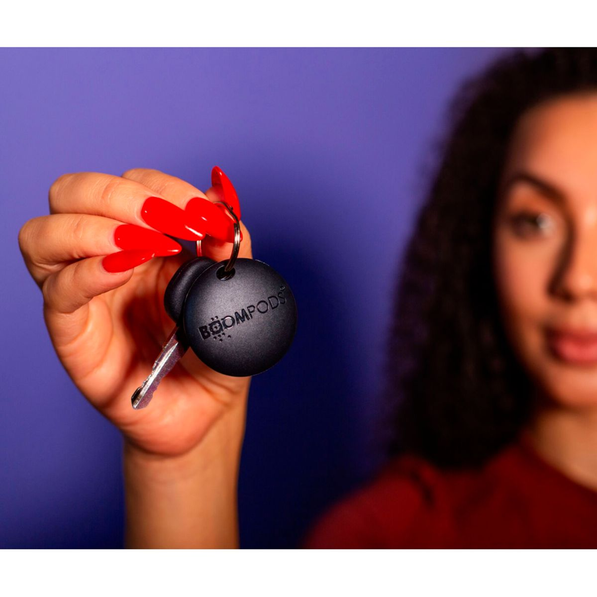 Kobieta trzyma klucz z czarnym brelokiem. Tło to fioletowa ściana.