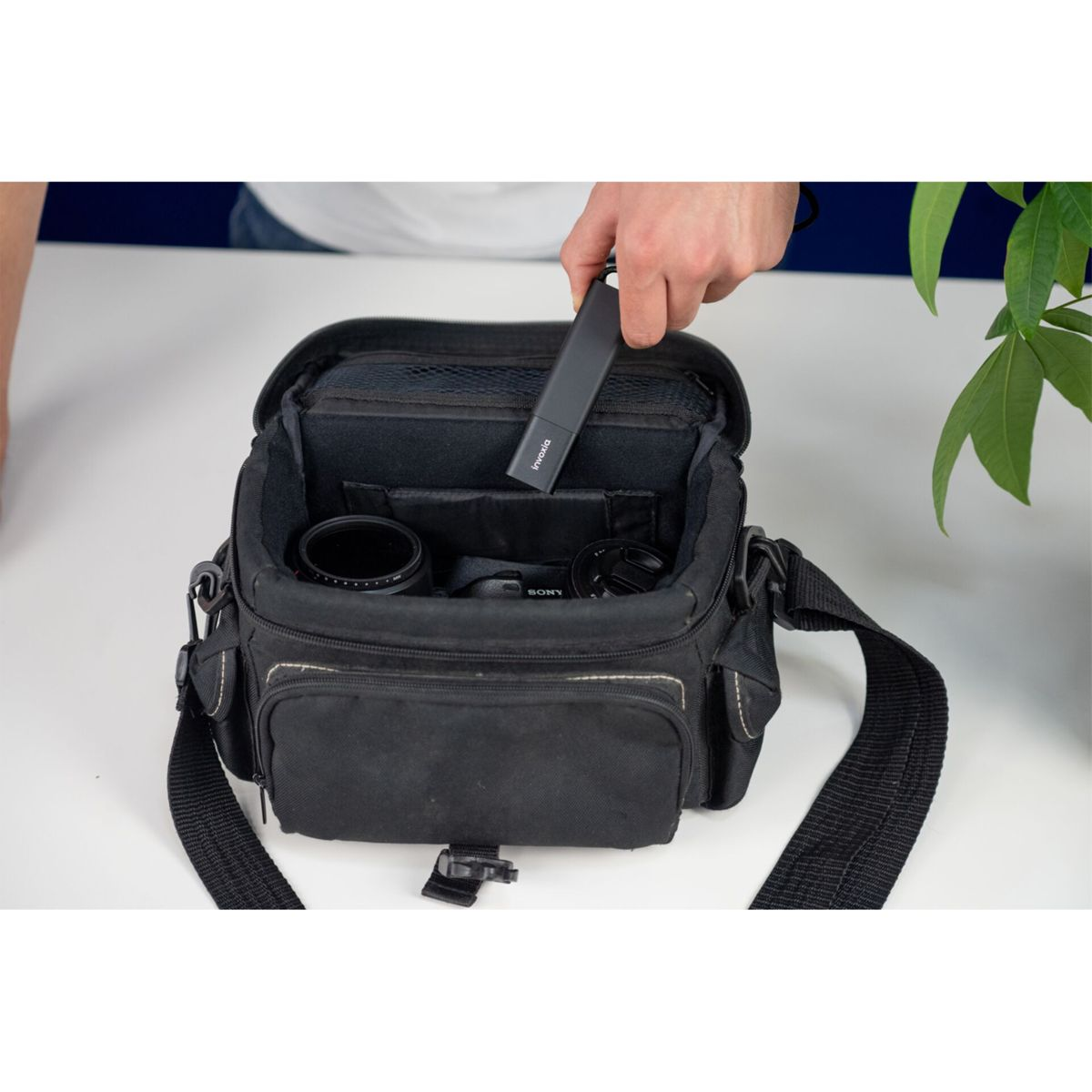 Osoba wyjmuje czarny pendrive z czarnej torby na aparat. Tło jest białe.