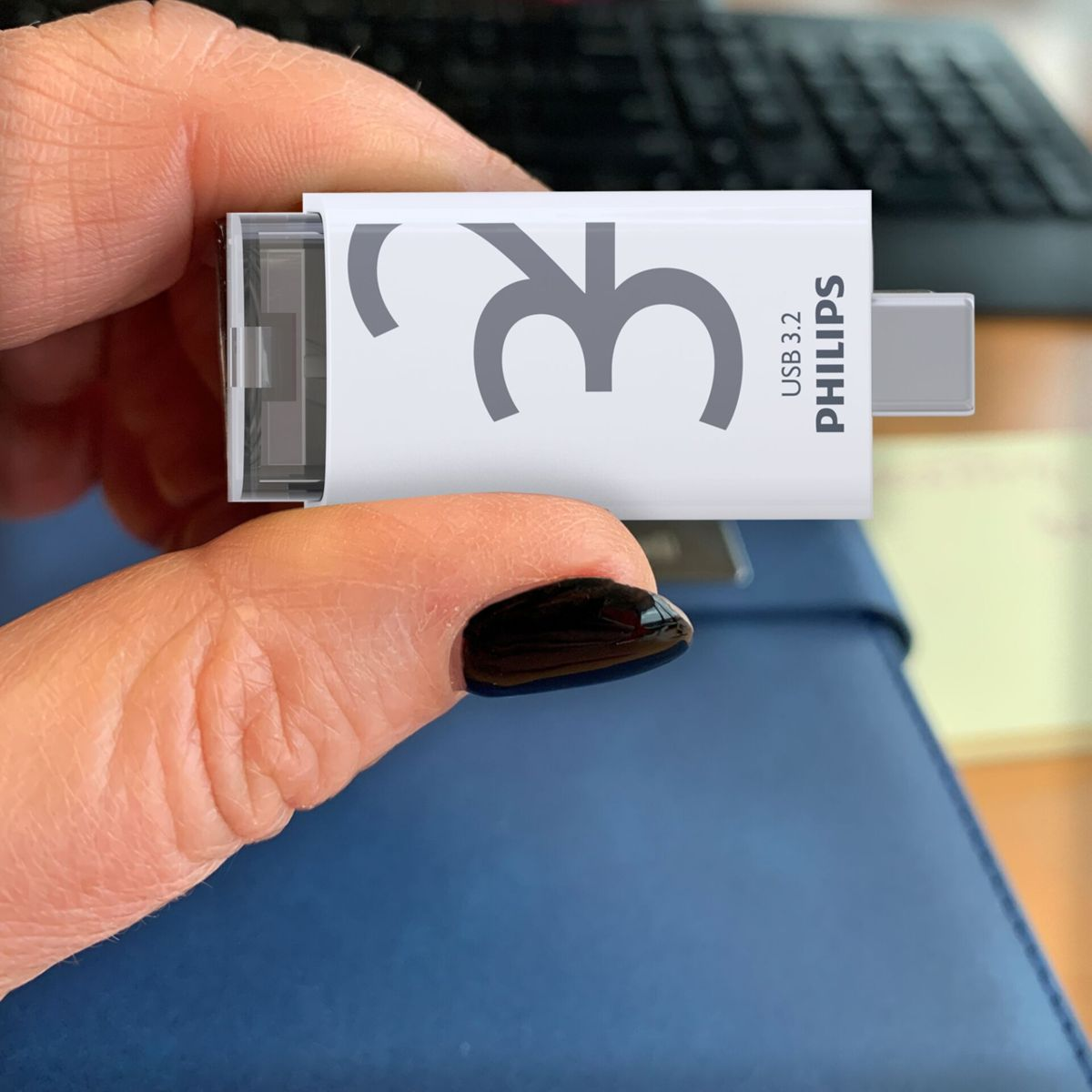 Ręka trzyma białą pamięć USB z napisem "3.2 USB PHILIPS". Pokazano niebieskie tło.