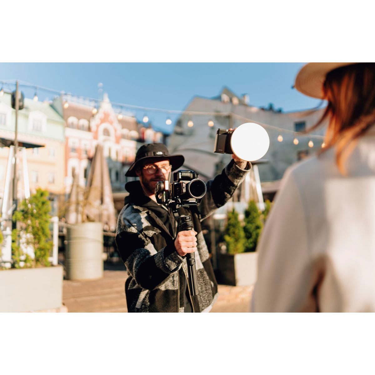 Ein Fotograf hält eine Kamera mit Lichtaufsatz und filmt eine Person. Der Hintergrund ist verschwommen.