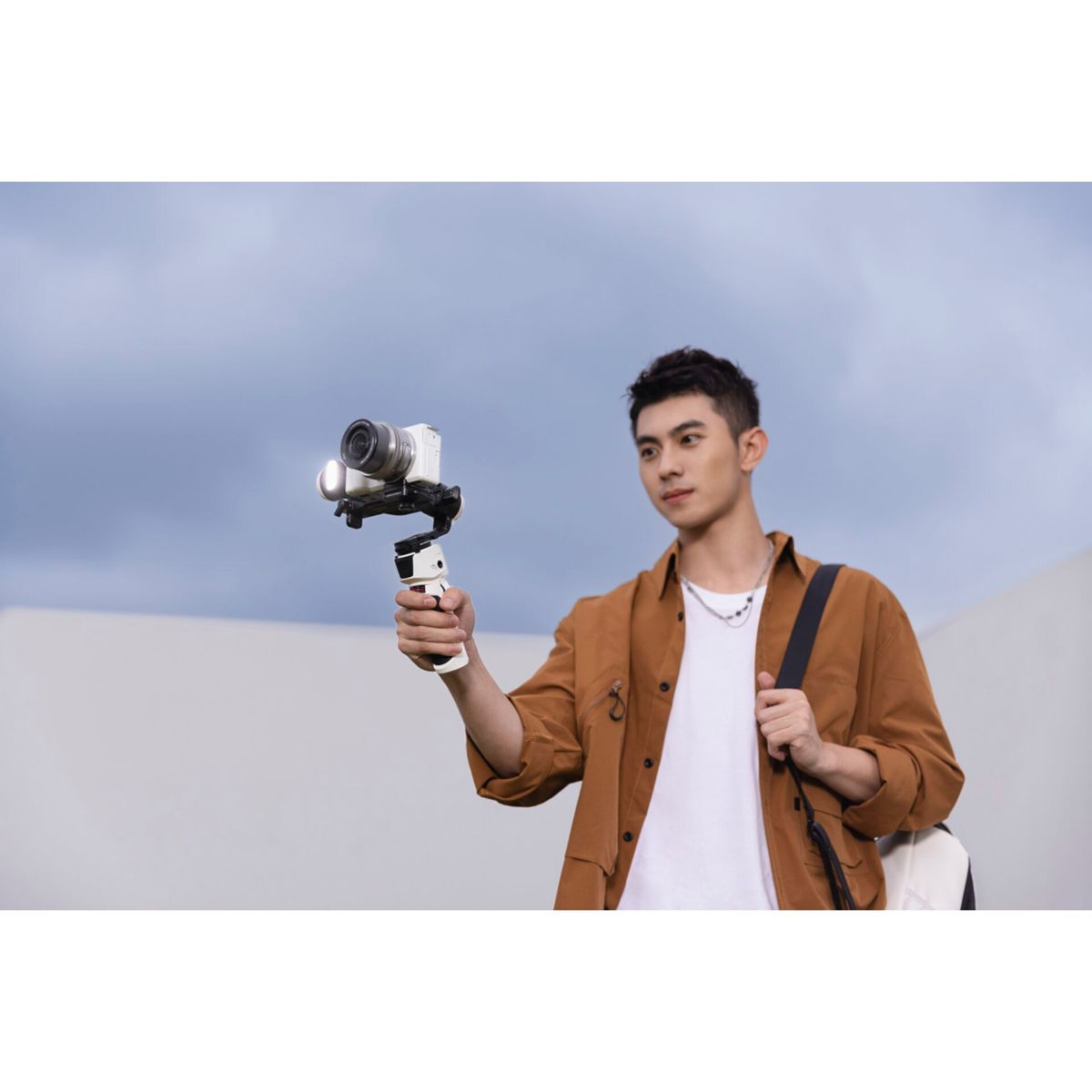 Ein Mann hält eine Kamera auf einem Gimbal und filmt. Er trägt eine braune Jacke und schaut in die Kamera.