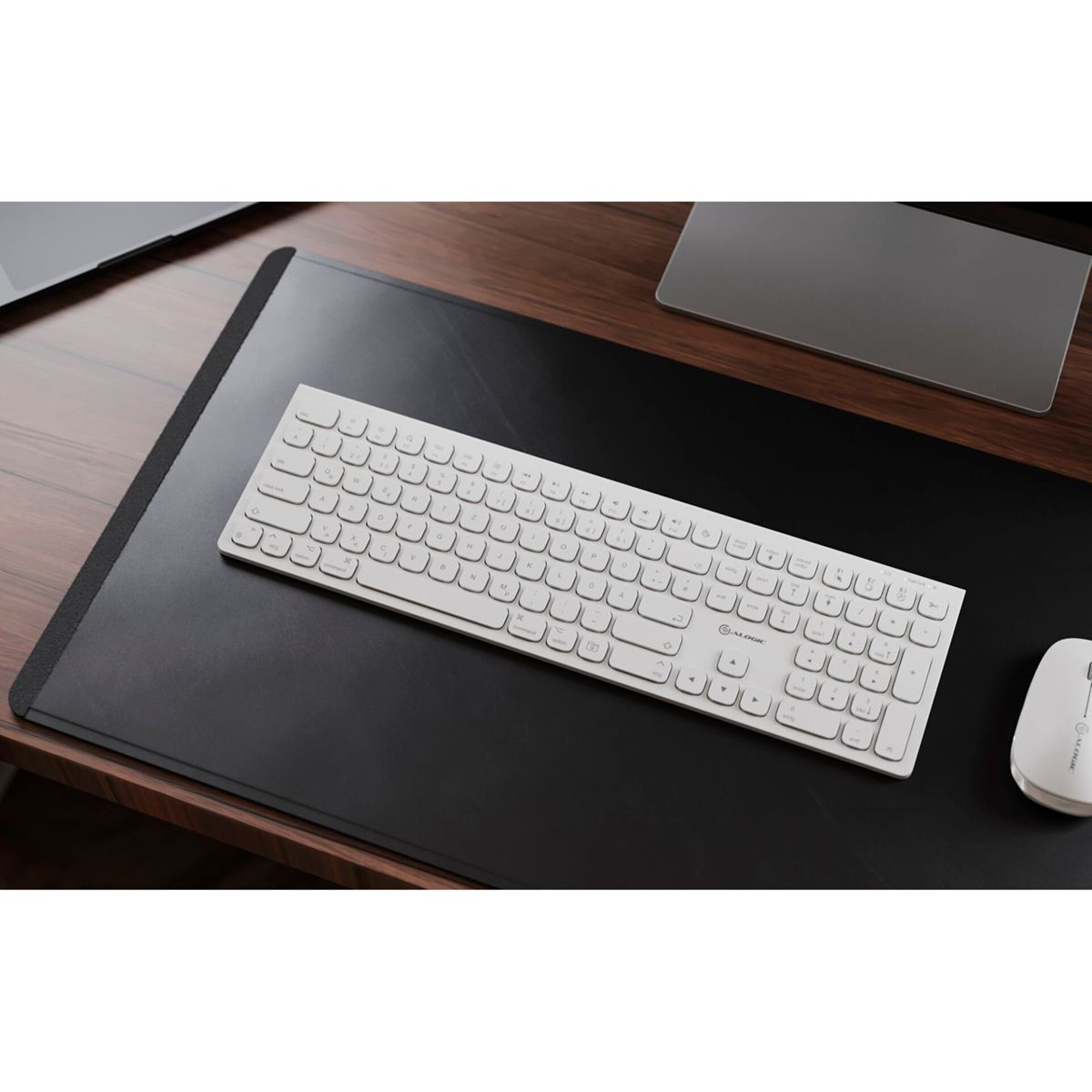 Weiße Tastatur auf einer schwarzen Schreibtischunterlage. Eine Maus und ein Laptop sind ebenfalls sichtbar.