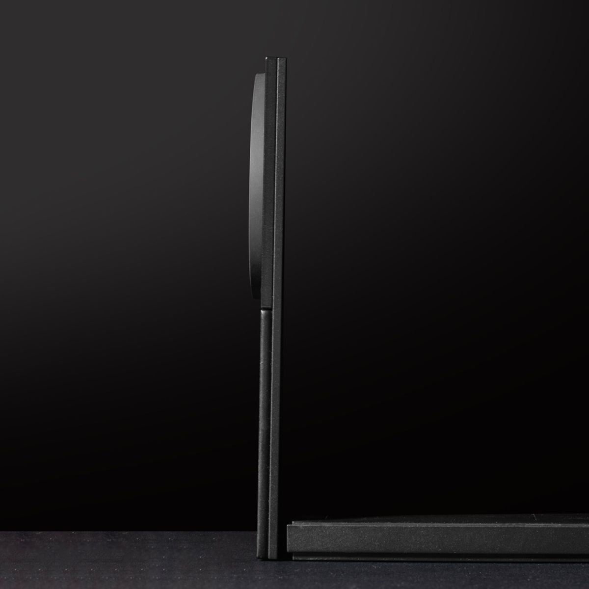 Ein dünner, schwarzer Monitor auf einer dunklen Oberfläche. Der Monitor wird von der Seite betrachtet, mit schwarzem Hintergrund.