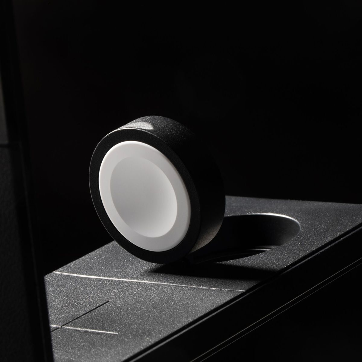 Un supporto di ricarica nero per Apple Watch, quadrante bianco e sfondo scuro.