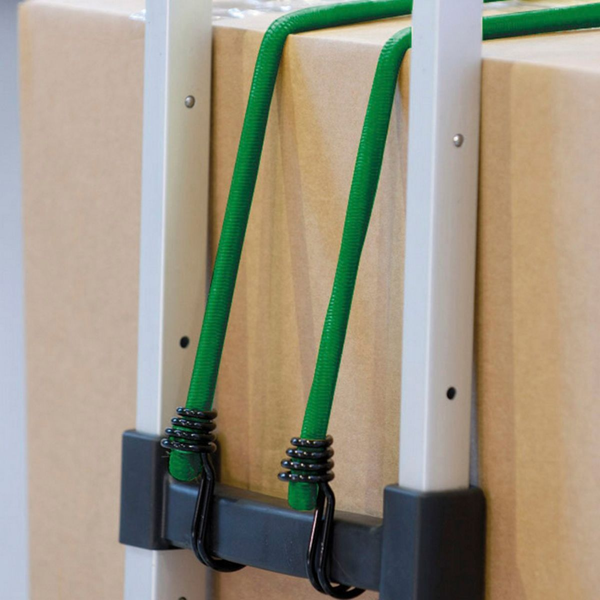 Primo piano di una scatola di cartone fissata a un carrello portabagagli con corde elastiche verdi. Il carrello è argentato con dettagli neri.