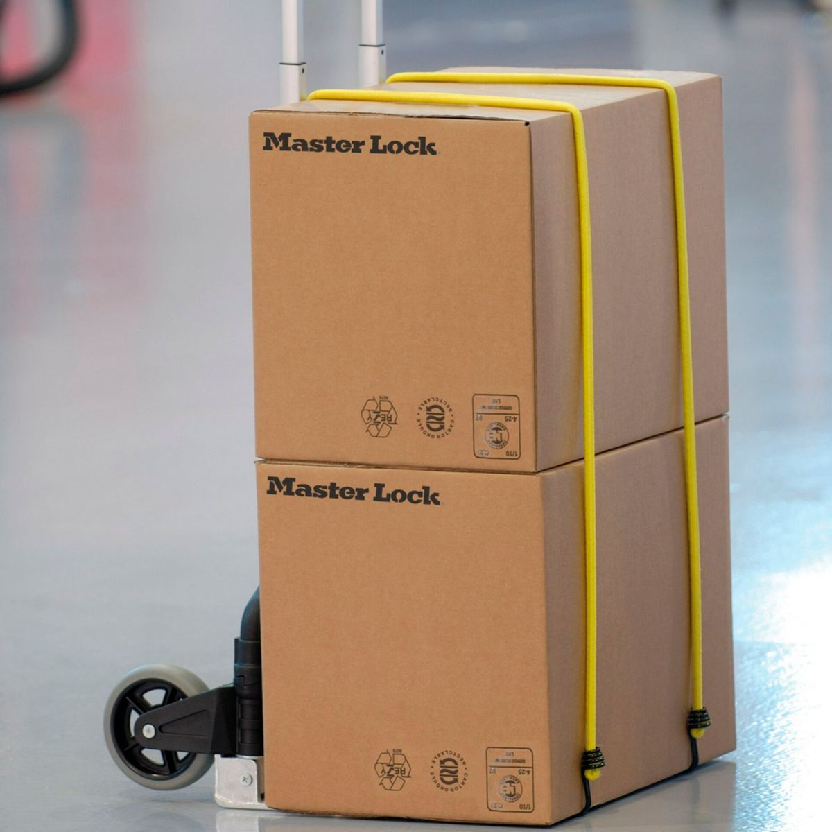 Due scatole di cartone, etichettate 'Master Lock', sono impilate su un carrello, fissate da una cinghia gialla.