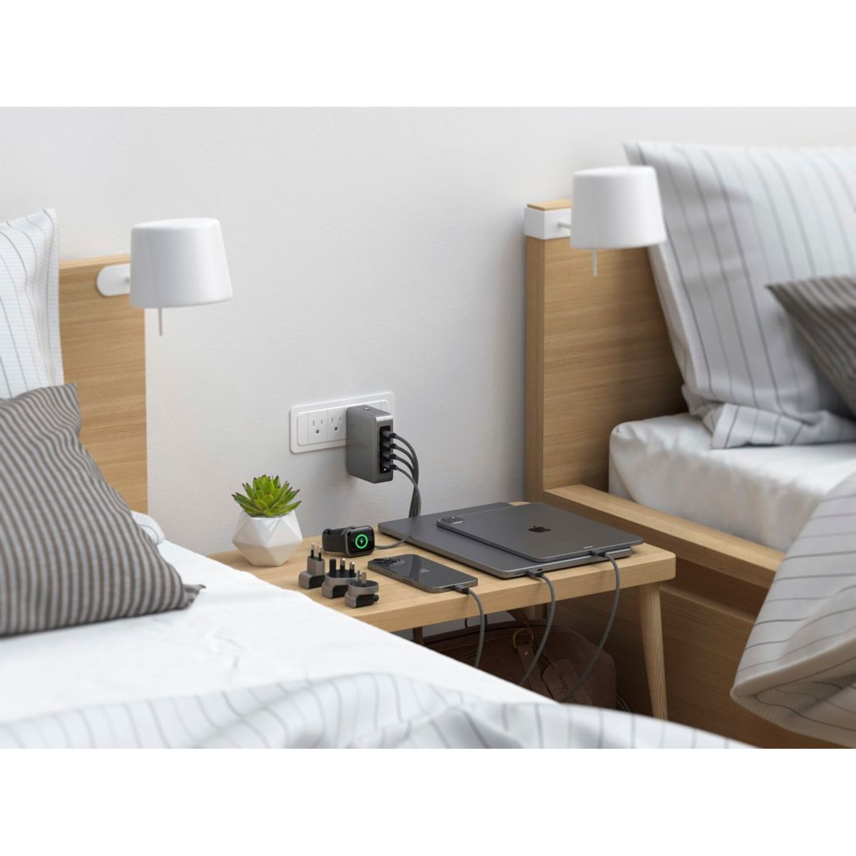 Scena del comodino con hub di ricarica, dispositivi e decorazioni. Include un laptop, un telefono e una piccola pianta.