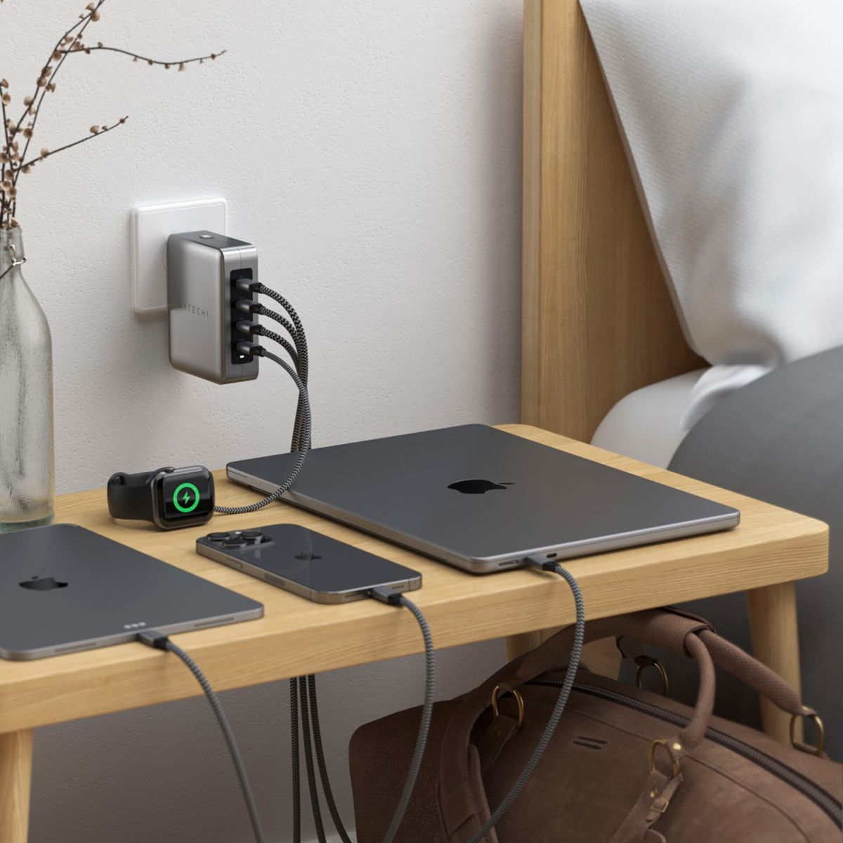 Comodino con caricatore, dispositivi e accessori. Include un laptop, un telefono, un orologio e una borsa.