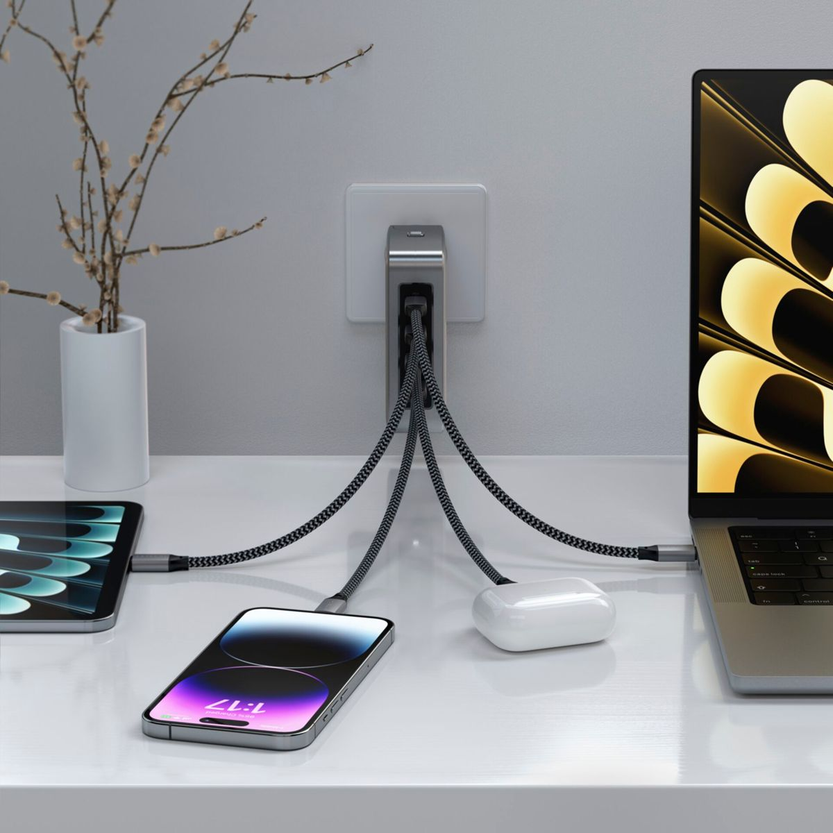 Un tavolo bianco con laptop, telefono, tablet e AirPods, tutti in carica da una fonte.