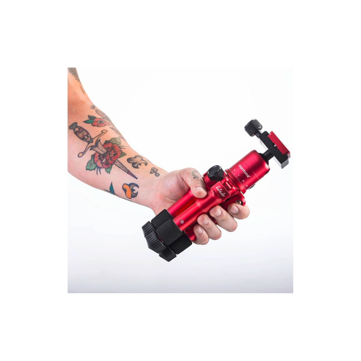 Ramię osoby z tatuażami trzyma czerwony statyw, ustawiony pod kątem. Statyw jest kompaktowy i ma czarne akcenty.