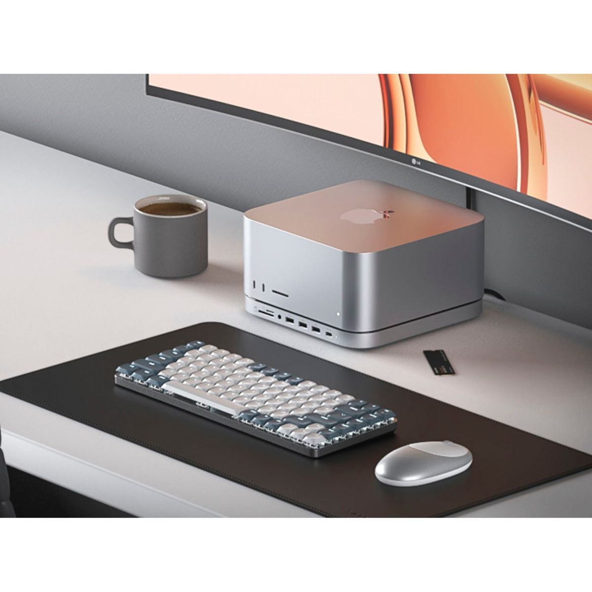 Ein silberner Computer, eine Tastatur und eine Maus auf einem Schreibtisch. Eine Tasse Kaffee ist auch vorhanden.