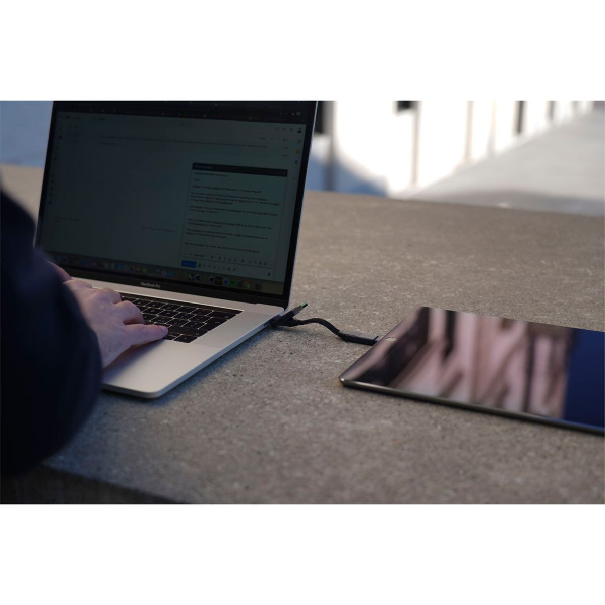 Un laptop collegato a un tablet su una superficie grigia. Una persona sta digitando sul laptop.