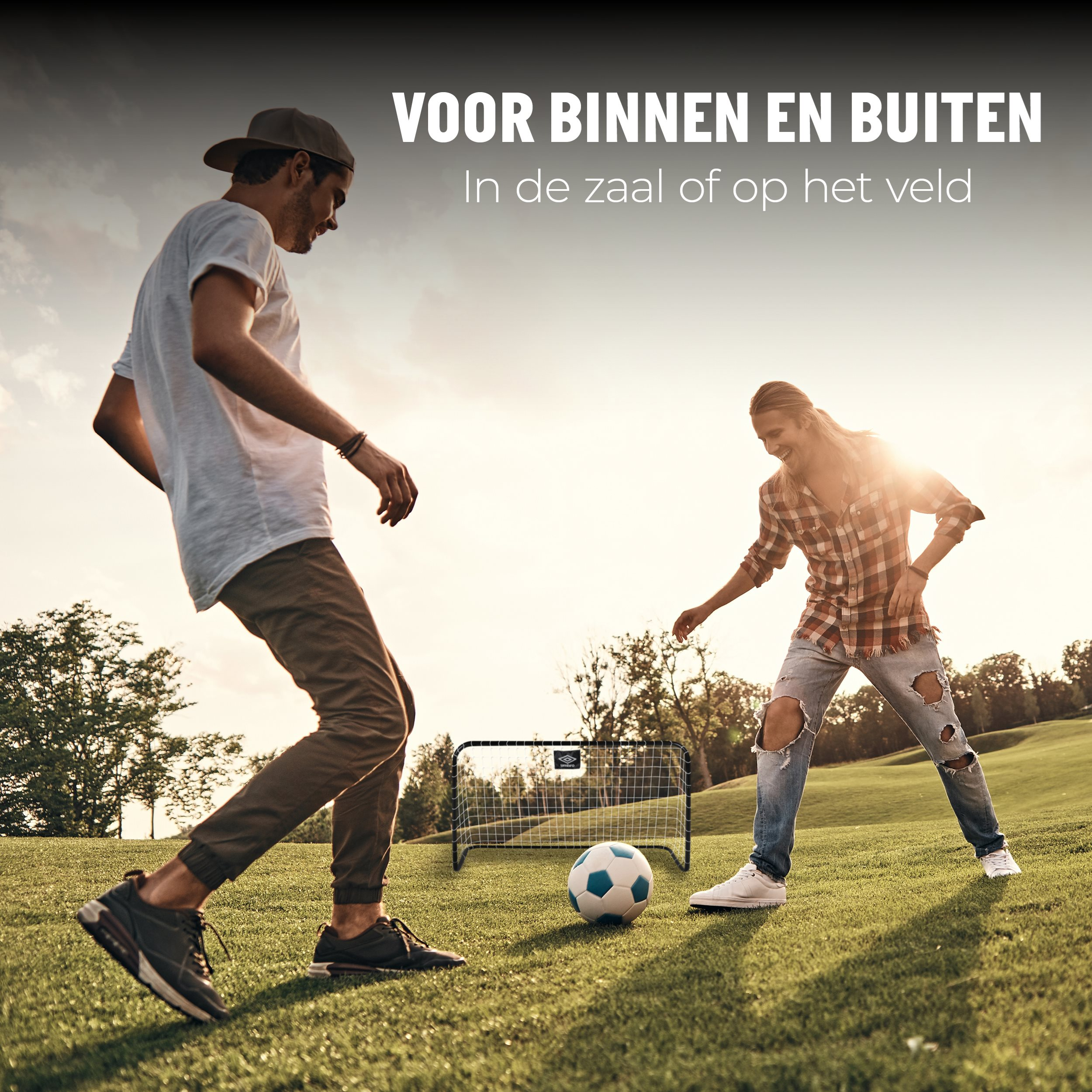 Zwei Personen spielen Fußball auf einem grünen Feld. Einer tritt den Ball. Im Hintergrund ist ein kleines Tor zu sehen.