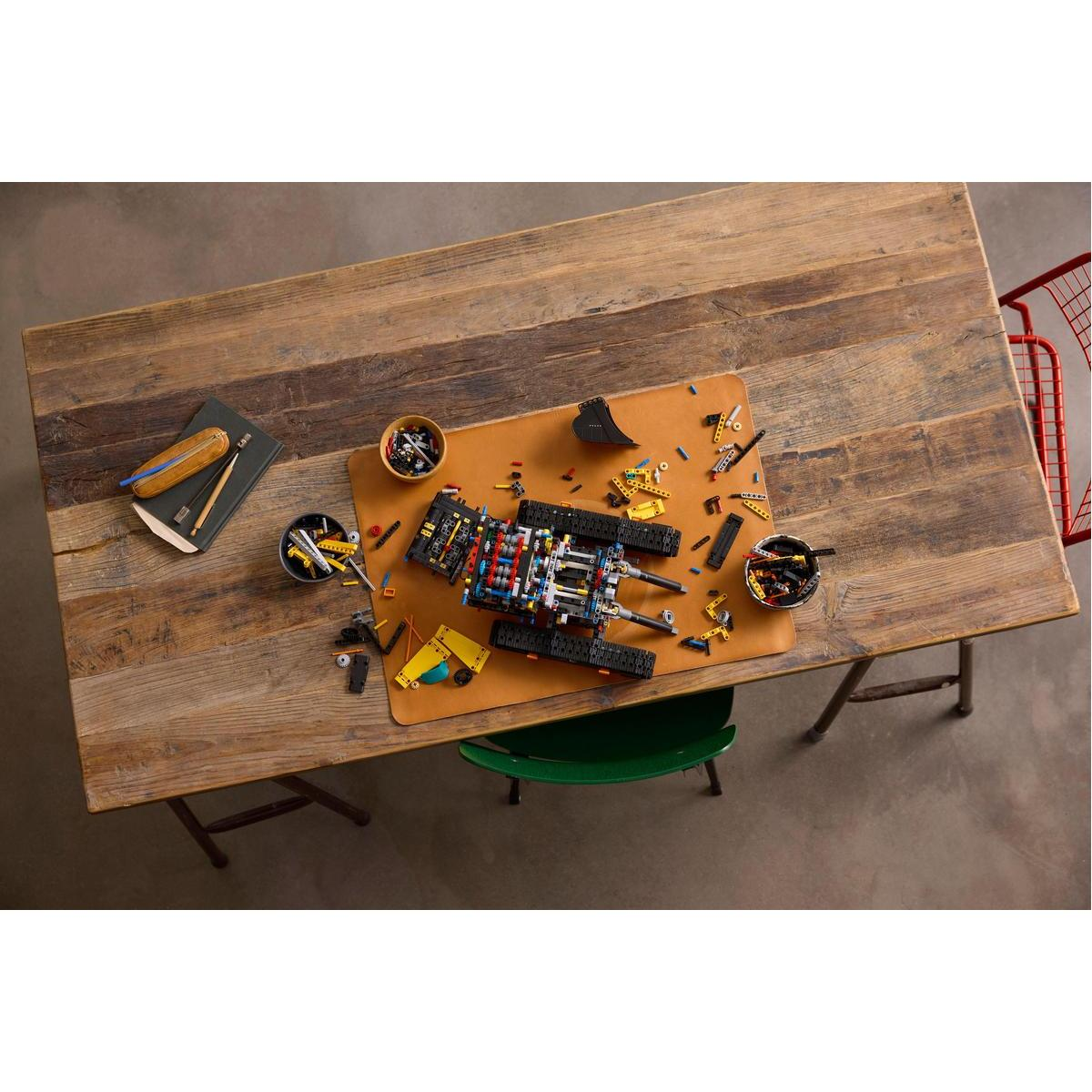 Widok z góry na części modelu Lego Volvo EC500 na drewnianym stole. Tor Lego i niedokończony model.