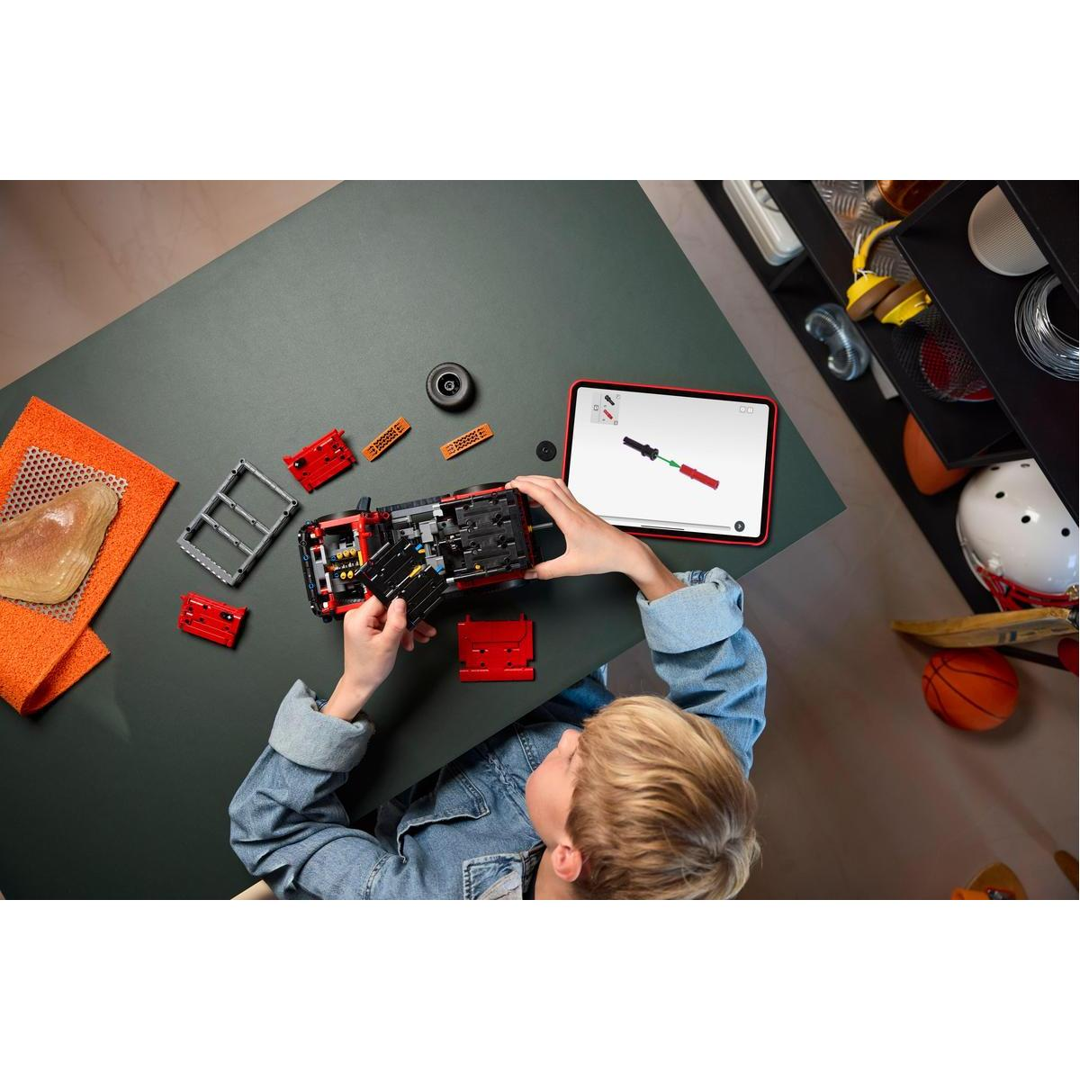 Osoba buduje czerwony samochód Lego z tabletem pokazującym instrukcje. Części i narzędzia na stole.