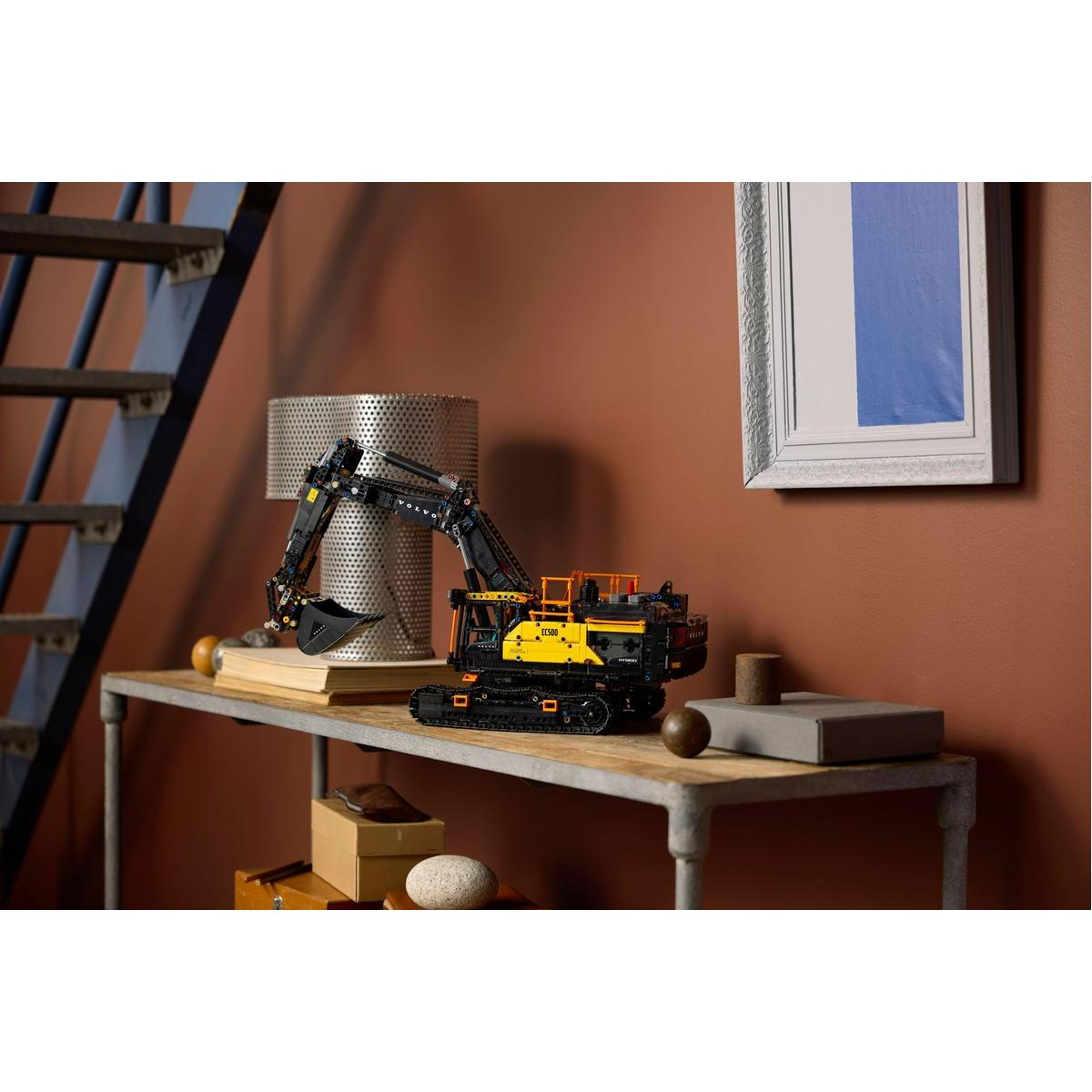 Model Lego Volvo EC500 na stole. Z tyłu obraz i schody.