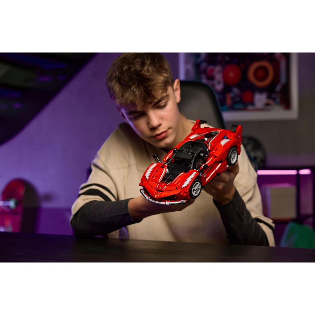 Osoba trzyma czerwony samochodzik. Samochód to model sportowy. Tło ma kolorową grafikę.