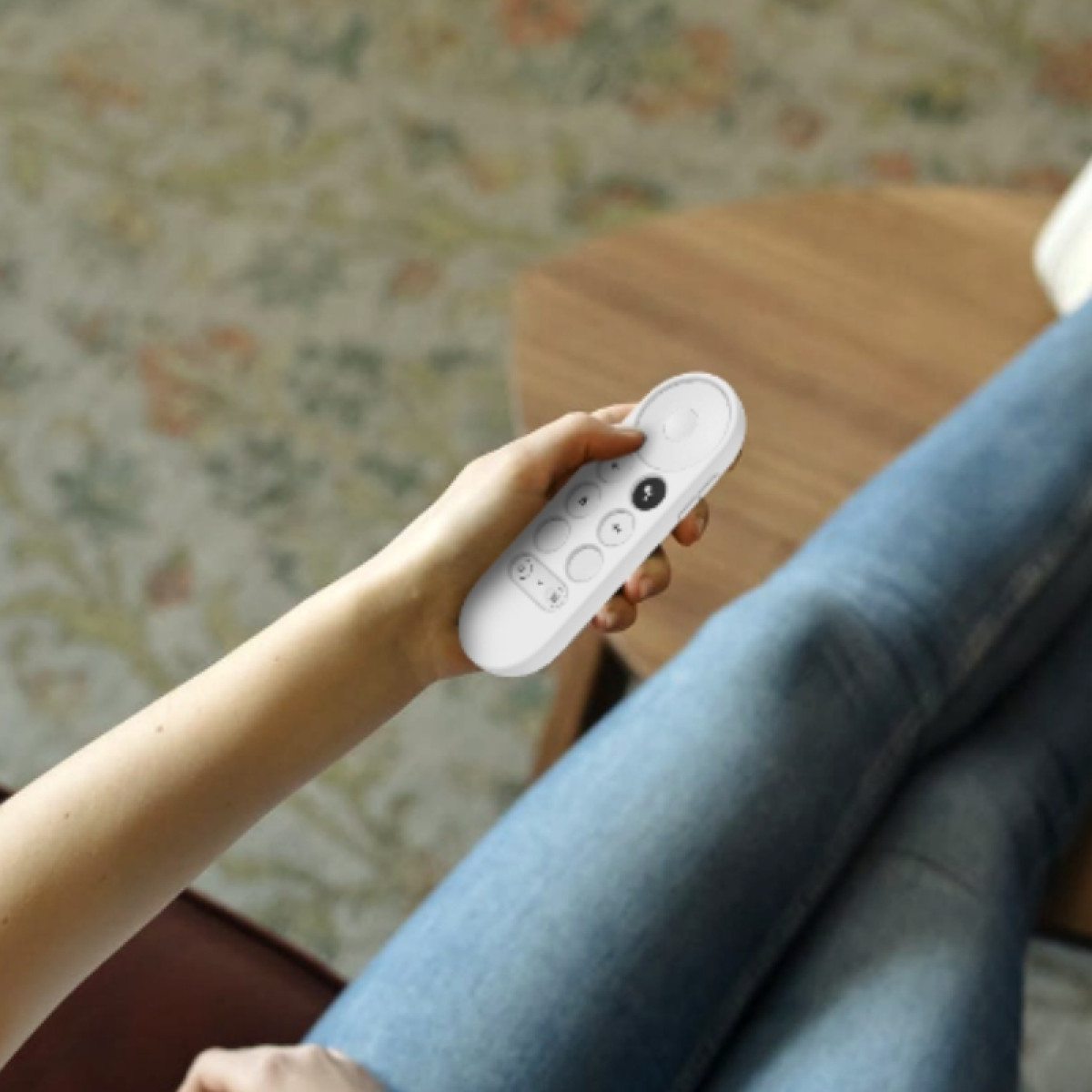Person hält weiße Fernbedienung mit Knöpfen, sitzt auf einem Sofa.