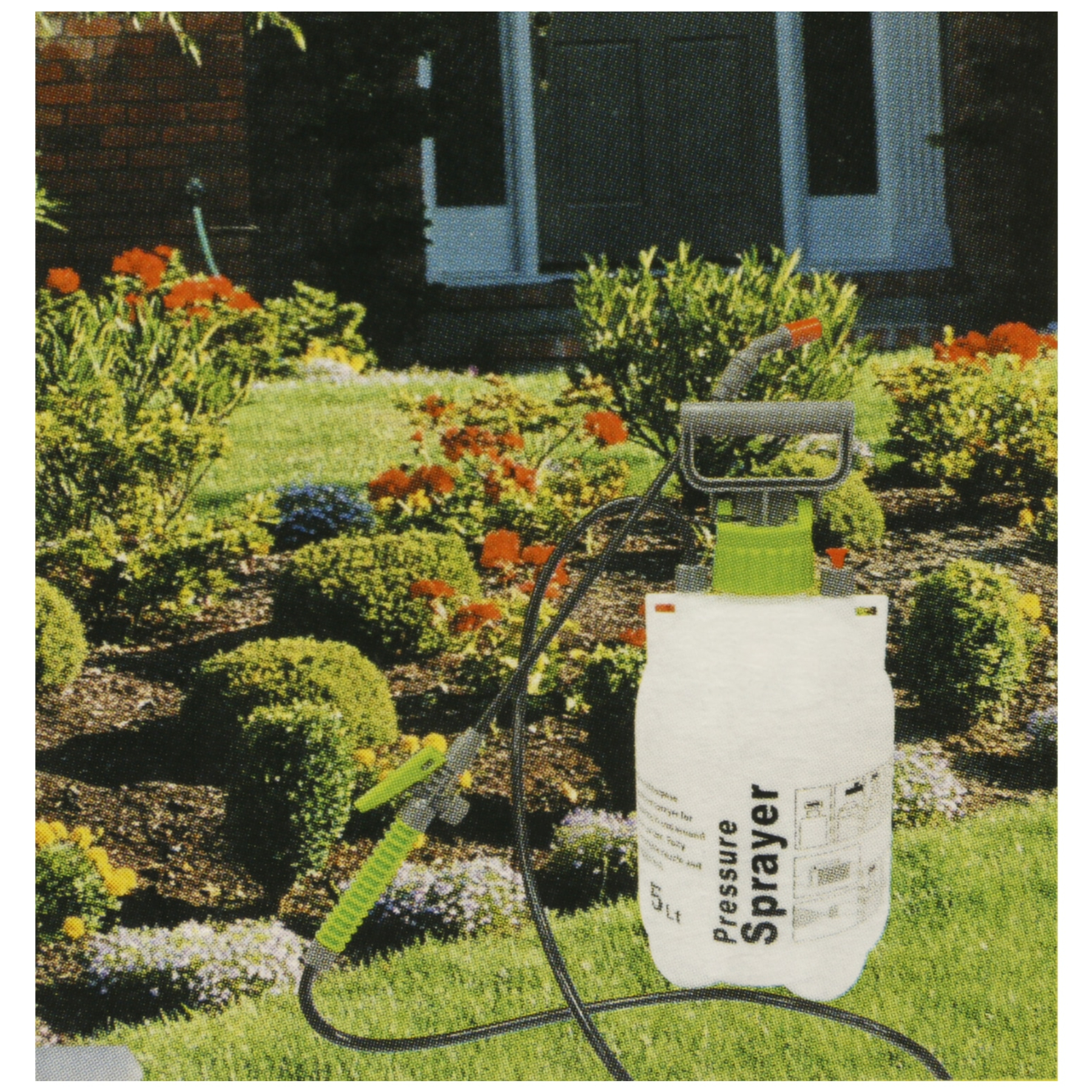 Een tuin met een witte drukpomp. Groene planten, bloemen en een huis op de achtergrond.