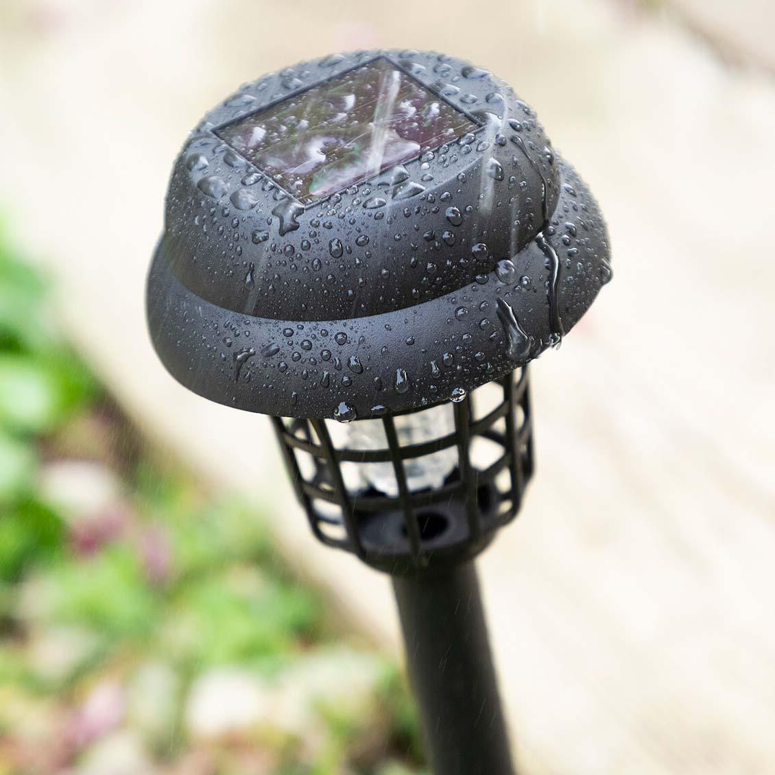 Primo piano di una lampada solare nera per zanzare. Gocce d'acqua sulla parte superiore. La luce è in gabbia e su un palo.