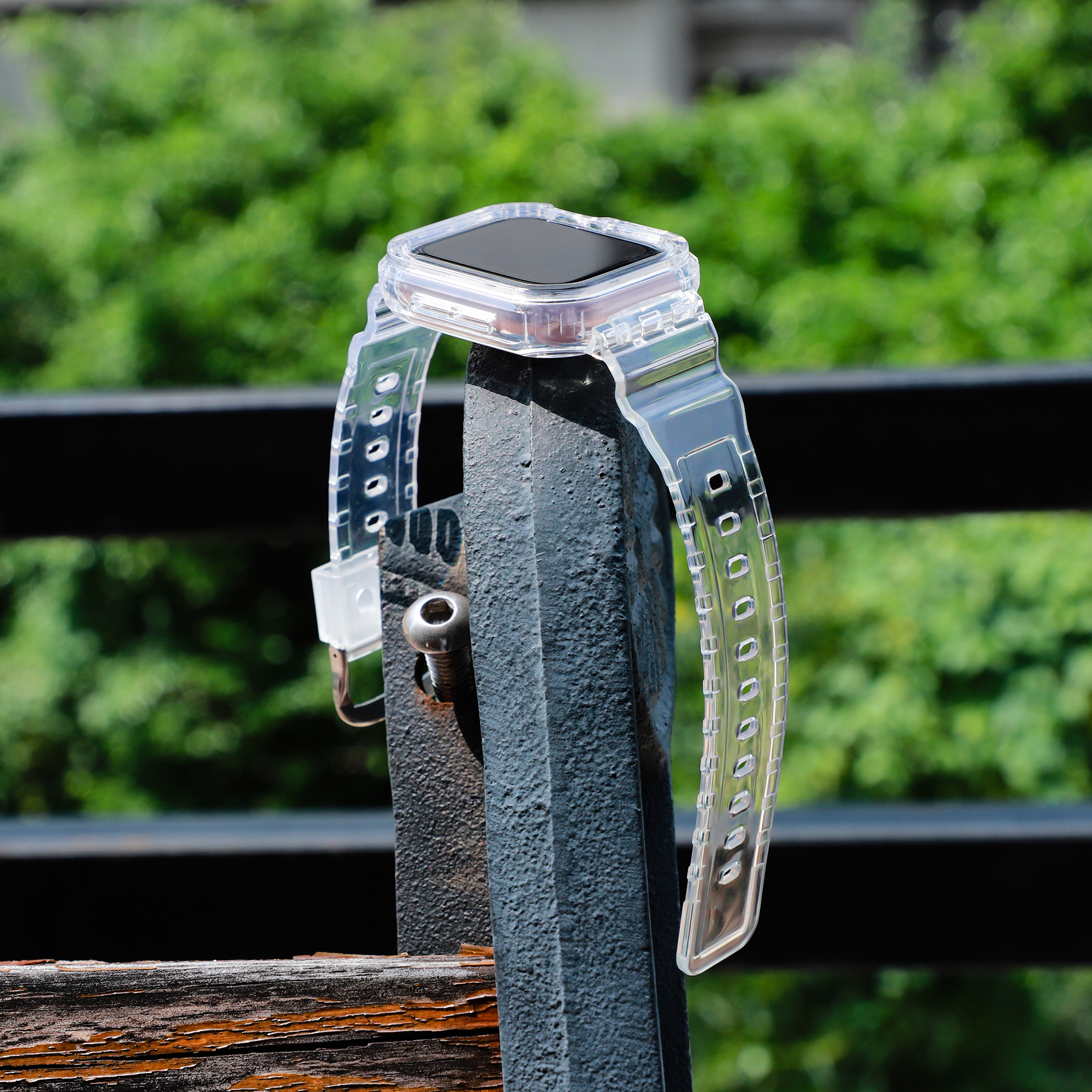 Eine transparente Smartwatch ist an einem schwarzen Metallpfosten befestigt. Der Hintergrund hat grüne Vegetation.
