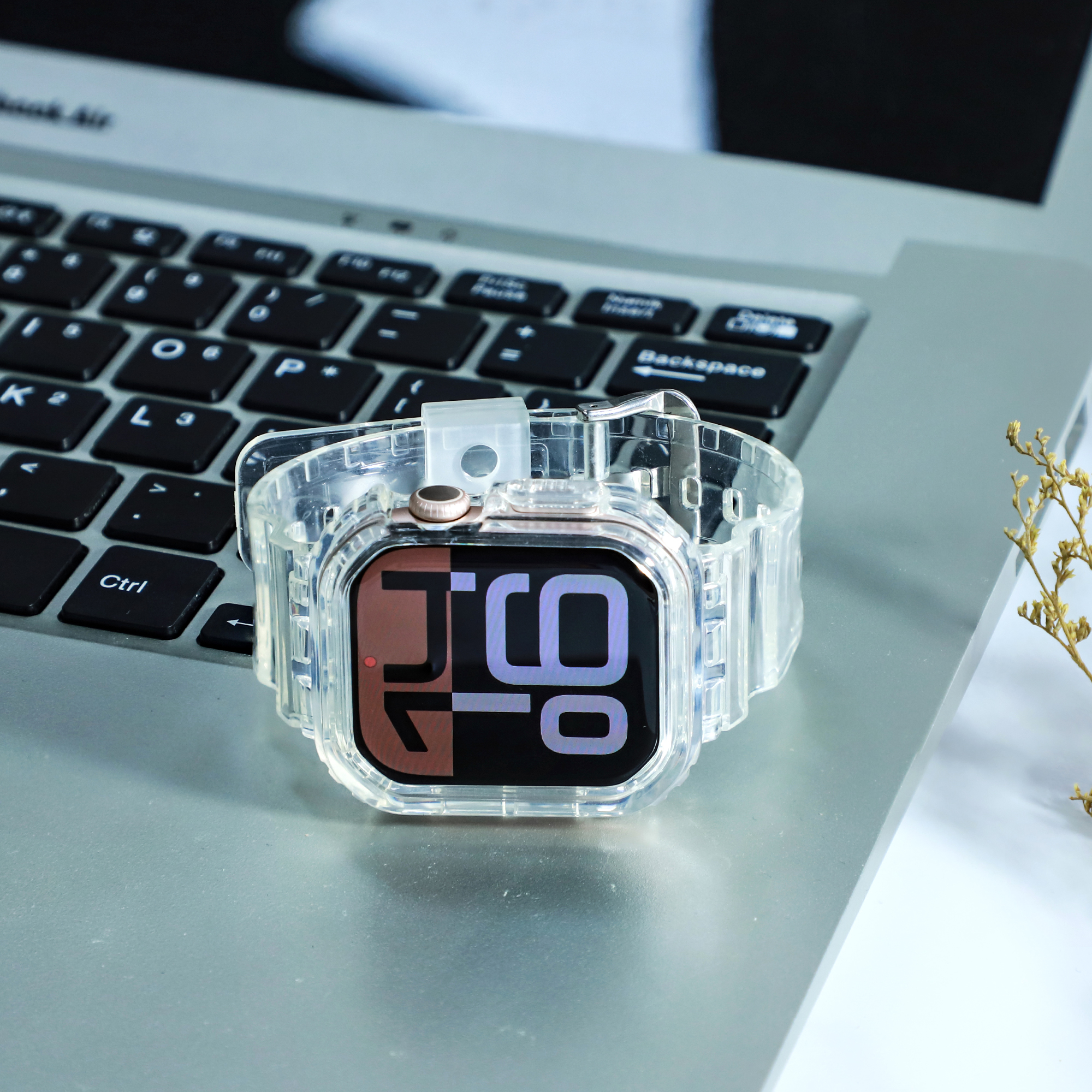 Eine klare Smartwatch auf einem Laptop. Das Zifferblatt zeigt die Uhrzeit, mit transparentem Armband und silbernem Rahmen.