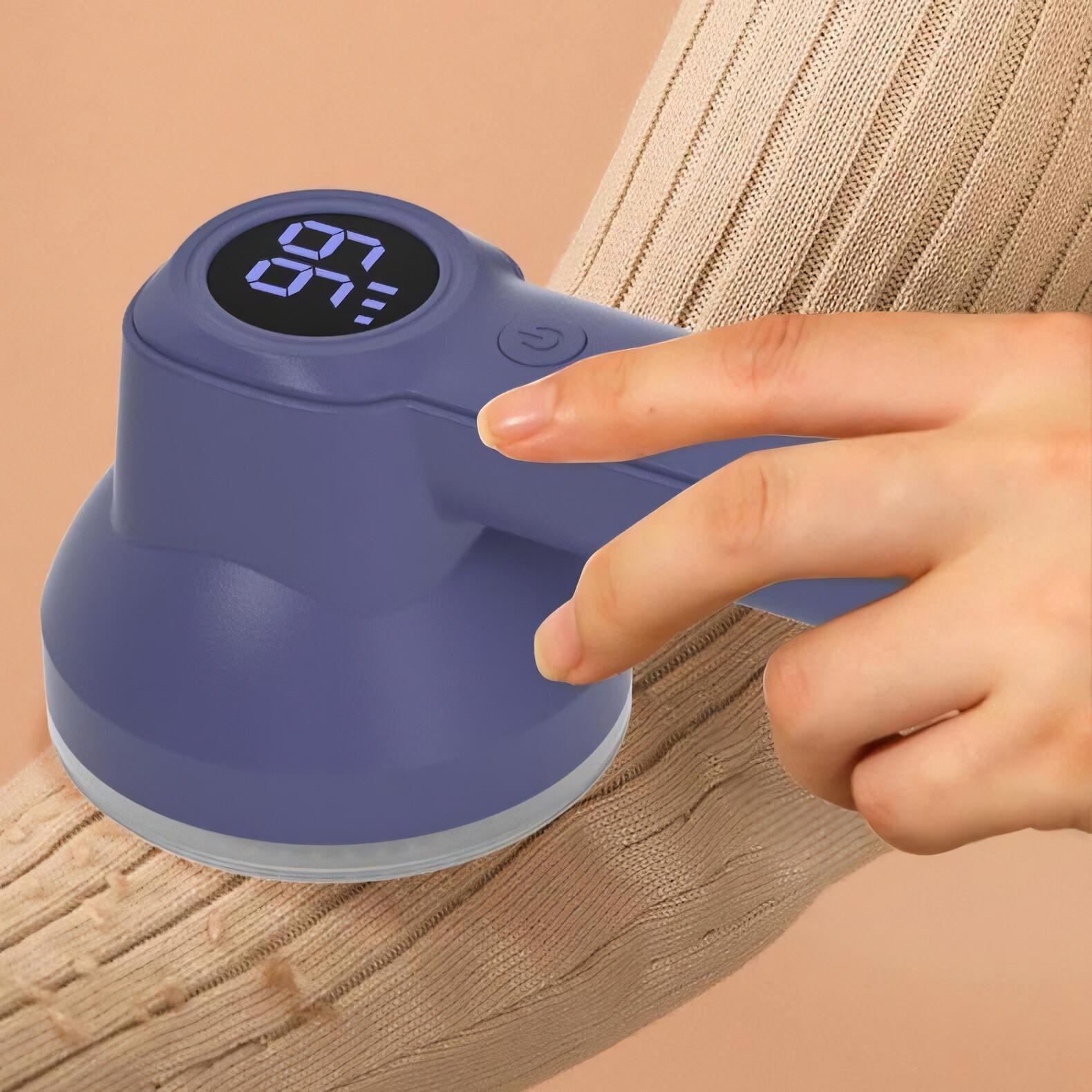 Eine Hand benutzt einen lila Stoffrasierer auf einem beigefarbenen Pullover. Der Rasierer hat oben eine Digitalanzeige.