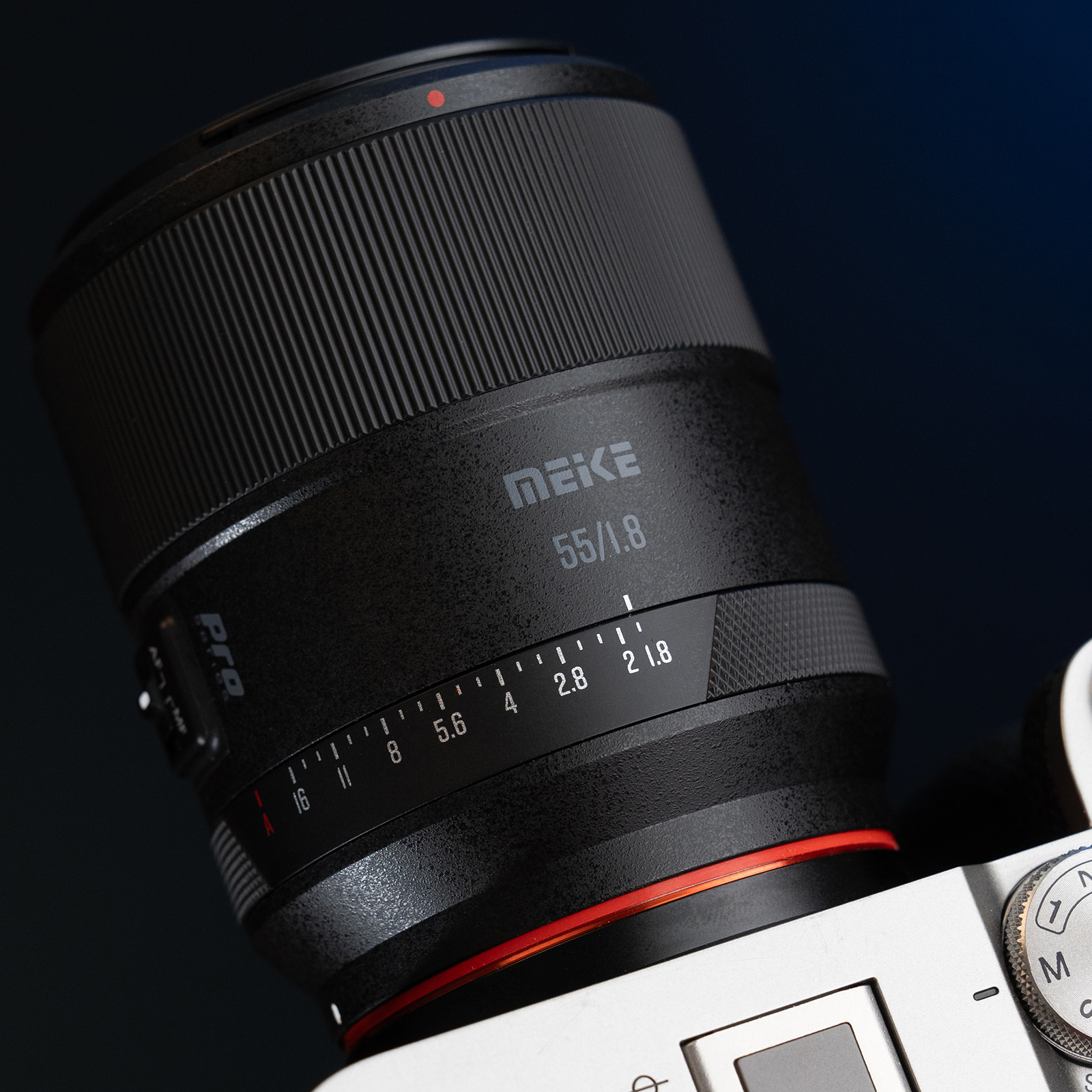 Schwarzes Kameraobjektiv mit 'MEKE 55/1.8'. Es ist abgewinkelt, mit rotem Ring und Blenden.