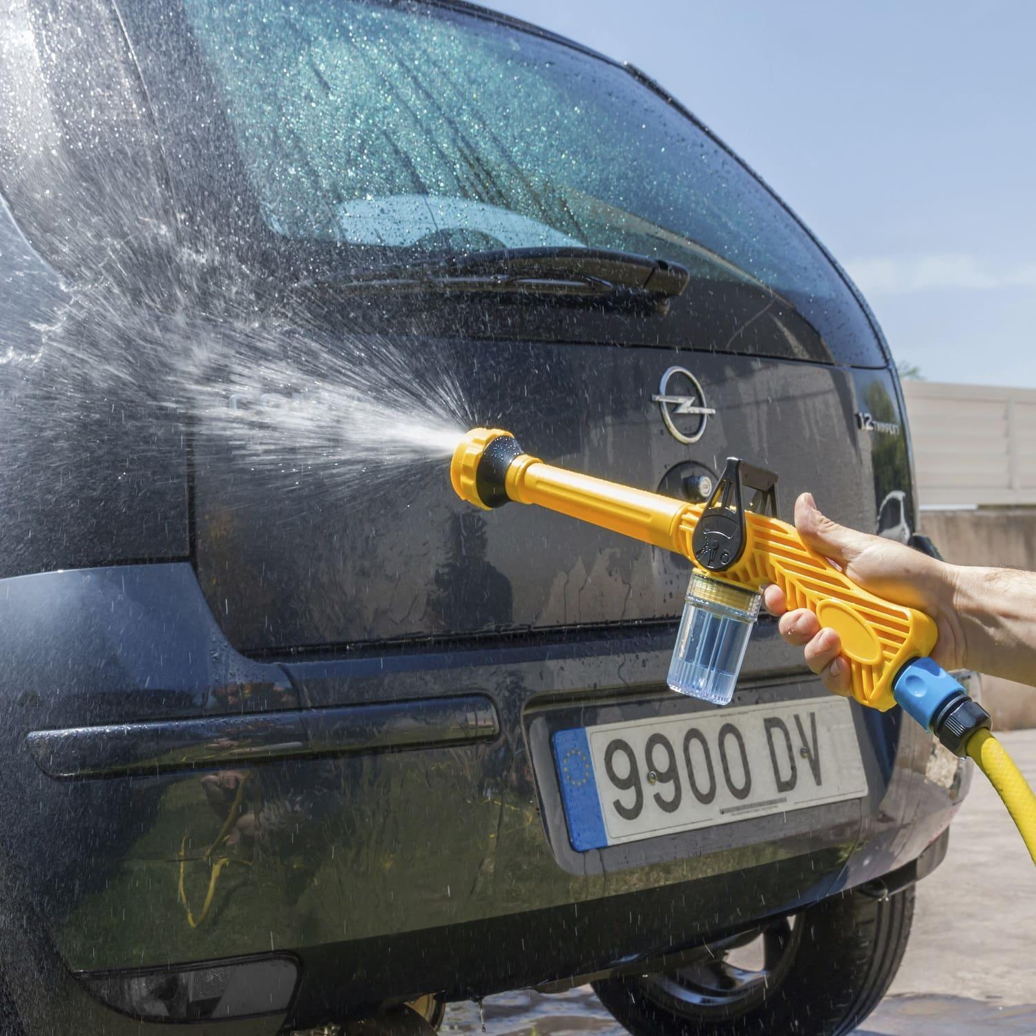 Ein gelber Wassersprüher sprüht Wasser auf die Heckscheibe eines schwarzen Autos.