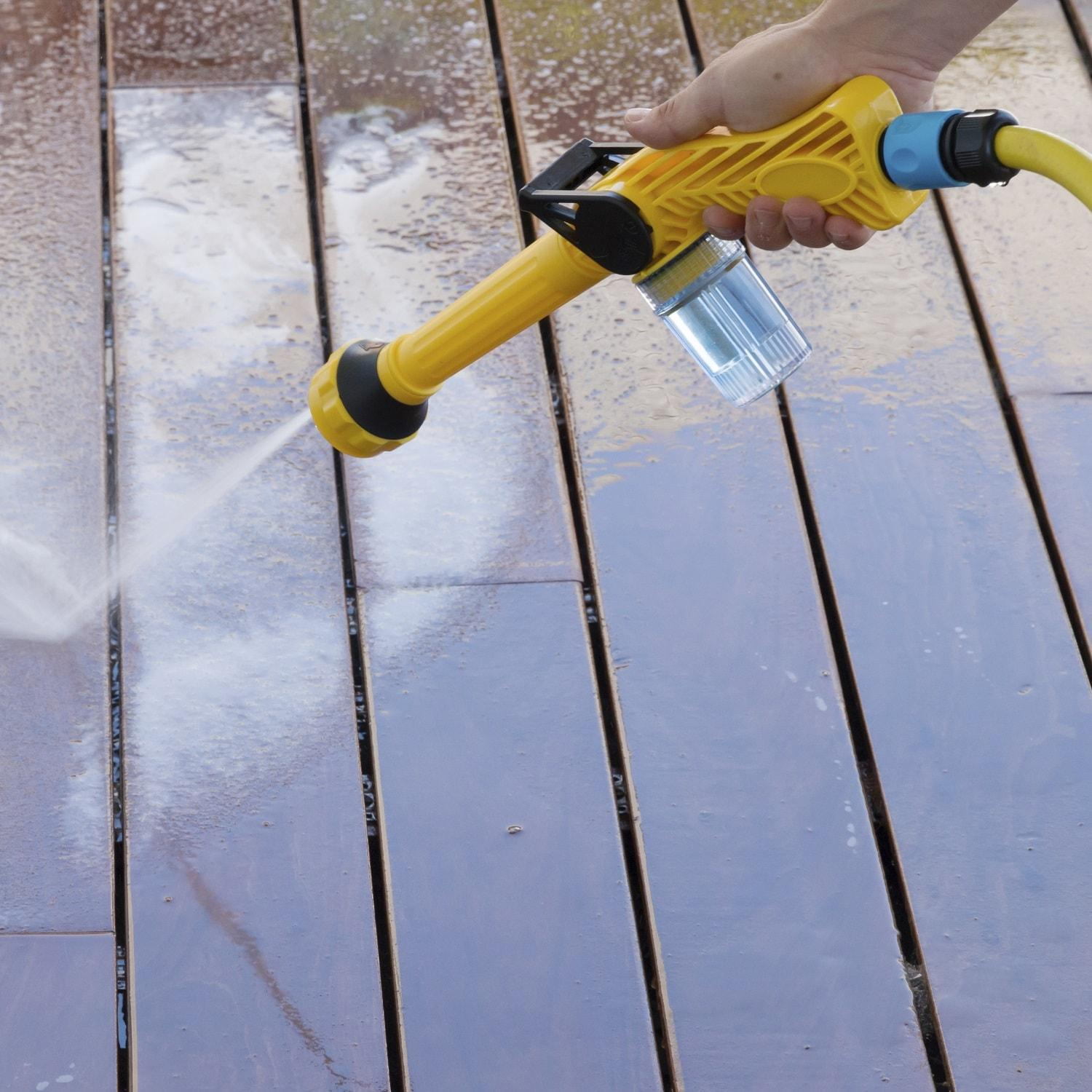 Eine Hand hält einen gelben Wassersprüher und besprüht ein Holzdeck.