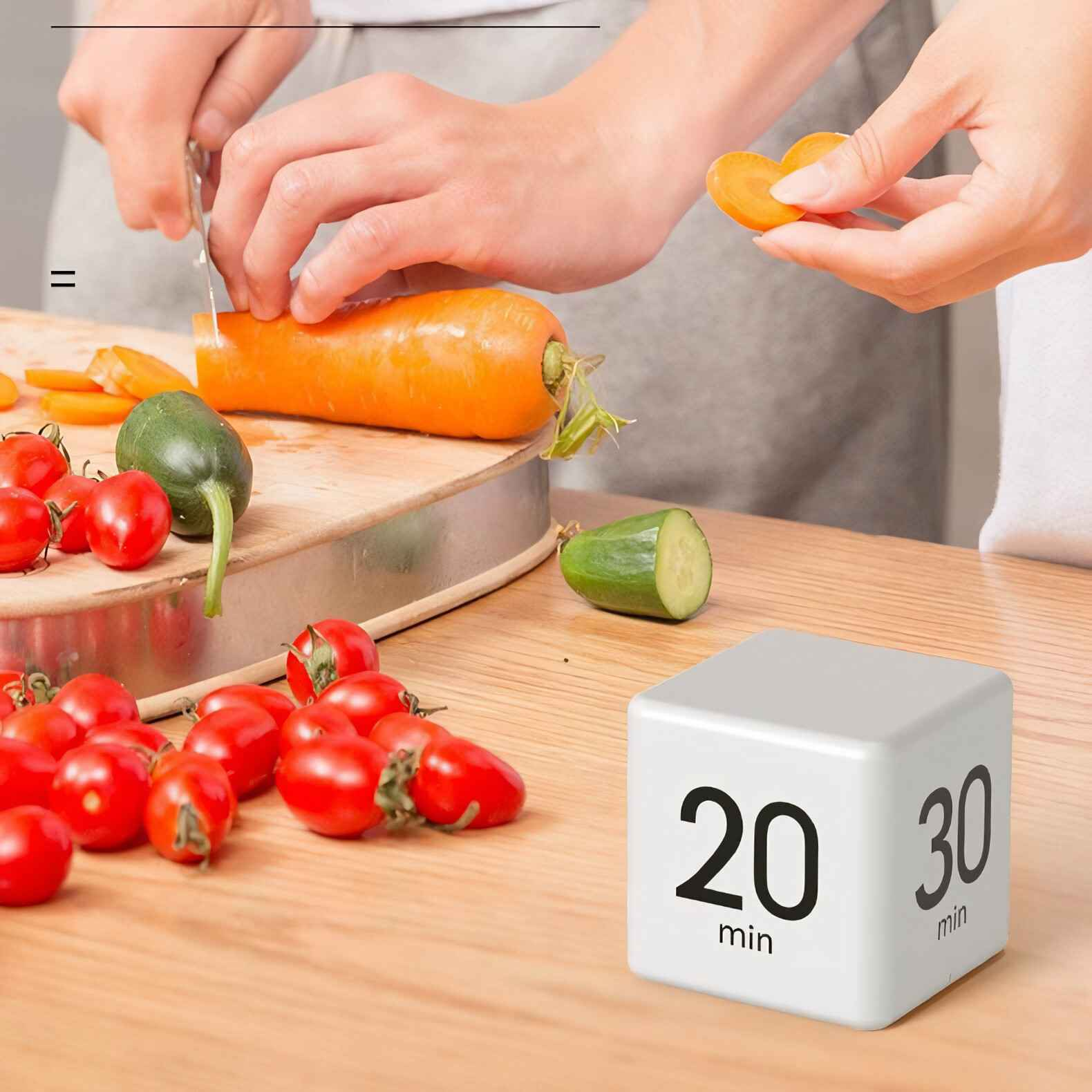 Eine Person schneidet eine Karotte, während ein Timer-Würfel auf einem Holztisch liegt, daneben Tomaten und Gurke.