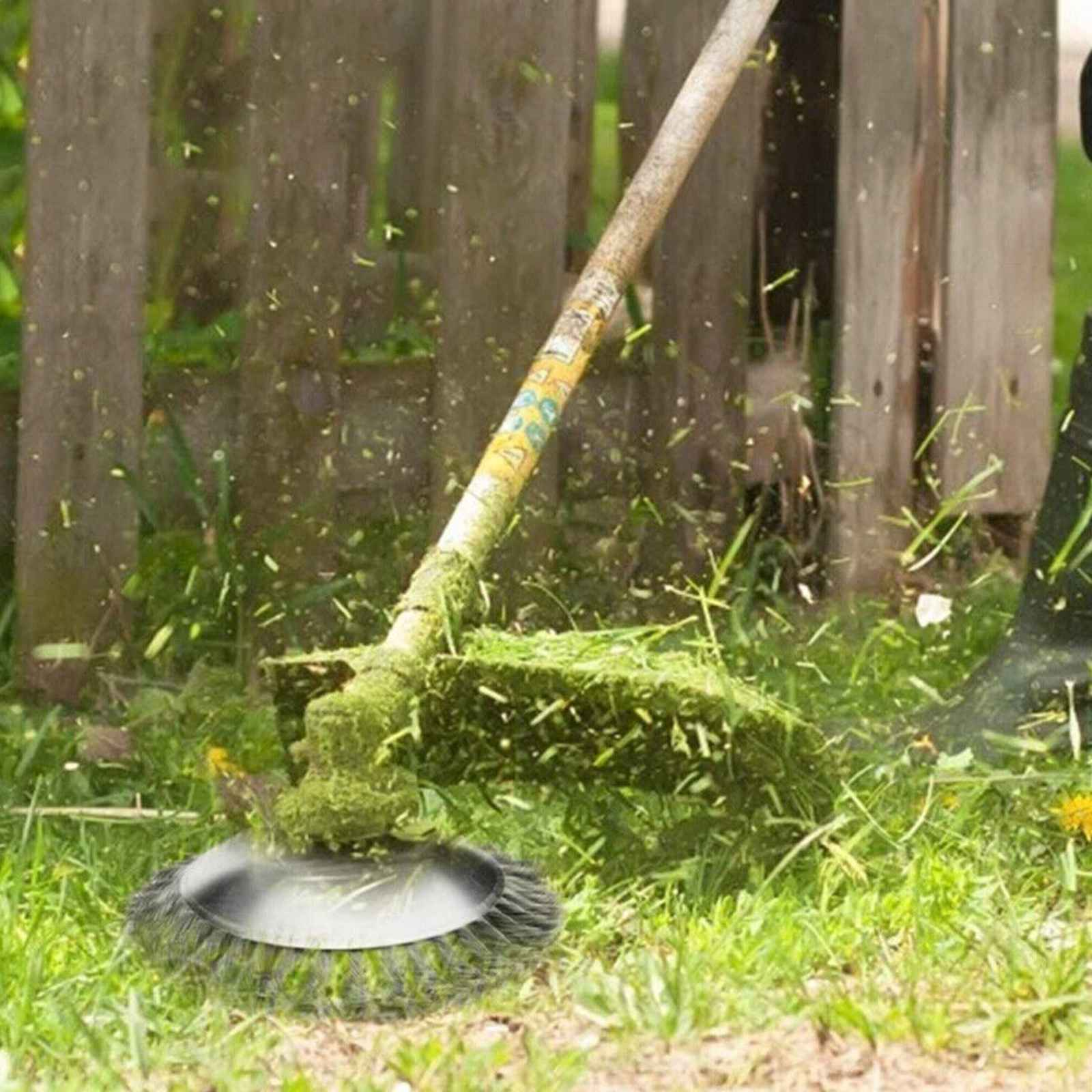 Ein Rasentrimmer schneidet Gras. Ein Metallkopf dreht sich und schneidet Gras. Grünes Gras und Holzzaun im Hintergrund.