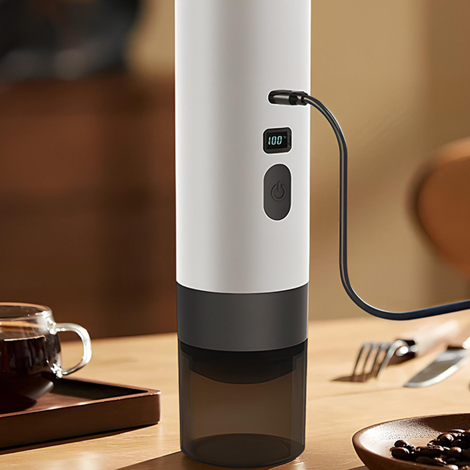Eine weiß-schwarze Kaffeemaschine mit Ladekabel, neben Kaffeebohnen.