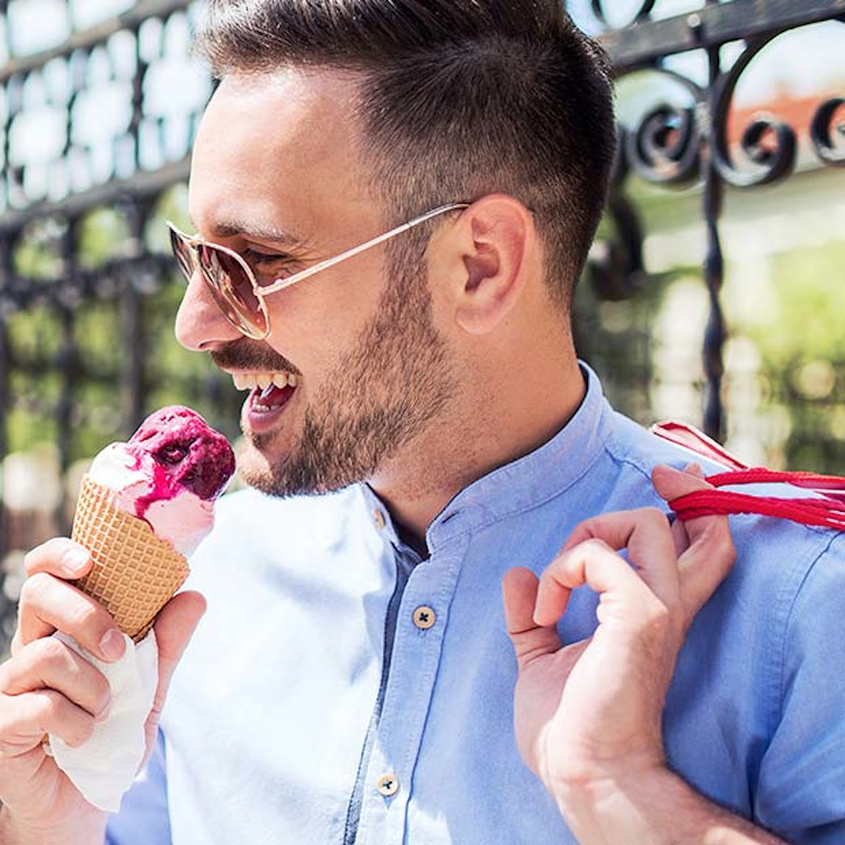 Ein Mann mit Sonnenbrille isst Eis aus einer Waffel. Er lächelt und hält einen roten Riemen.