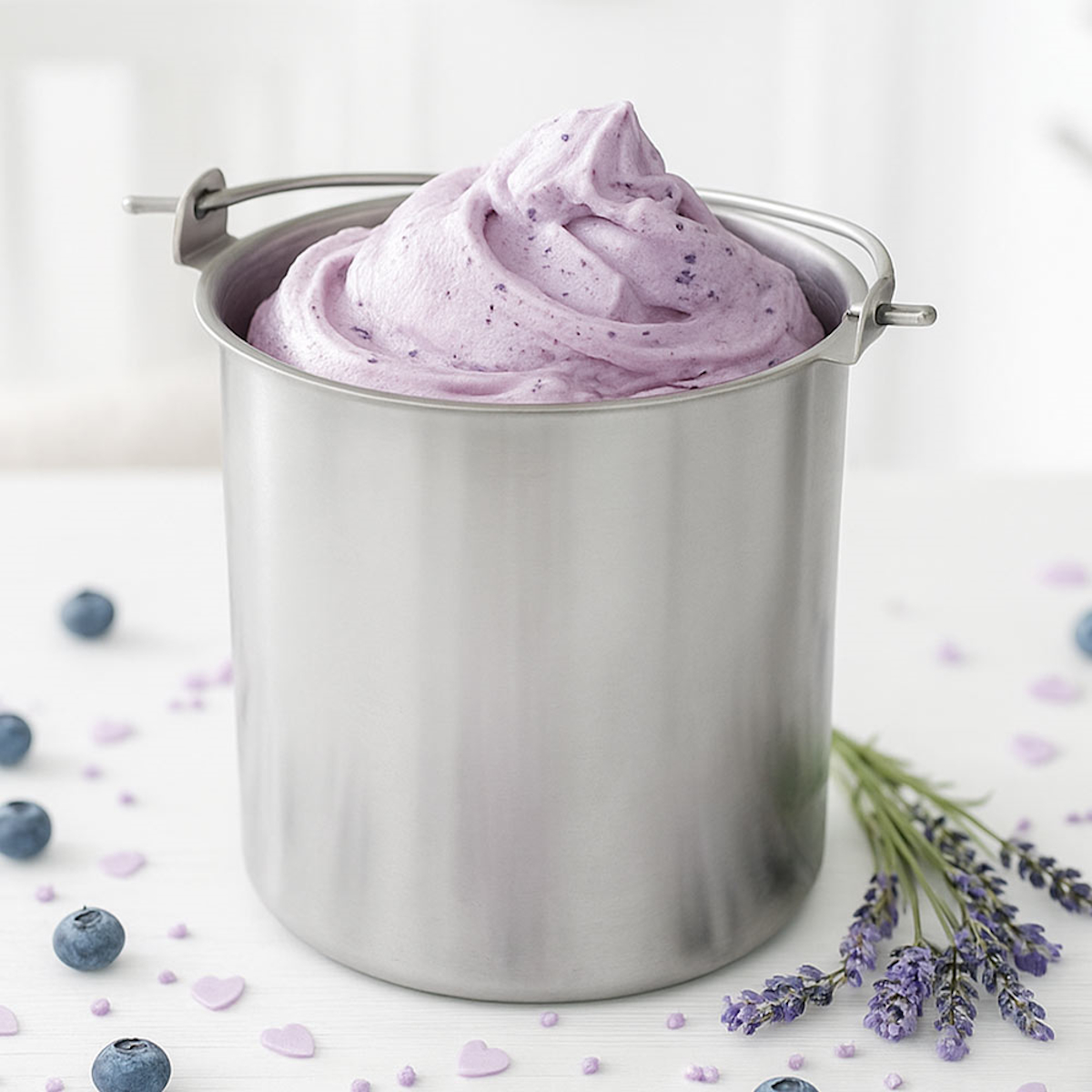 Ein Edelstahlbehälter ist mit violettem Eis mit Blaubeeren gefüllt. Lavendel und Herzen sind darum herum.