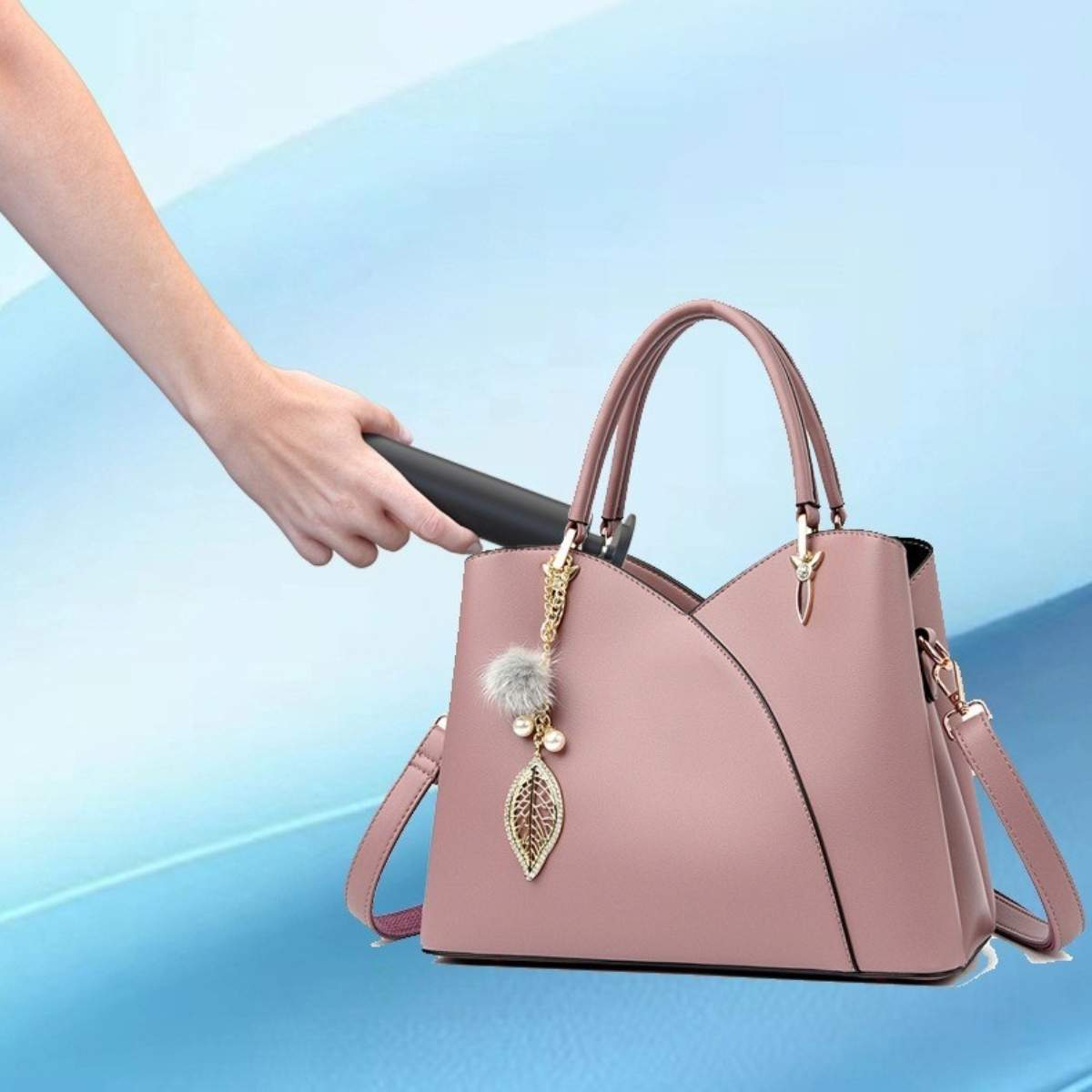 Die Hand einer Frau greift nach einer rosa Handtasche mit einem Blattanhänger und einem flauschigen Ball.